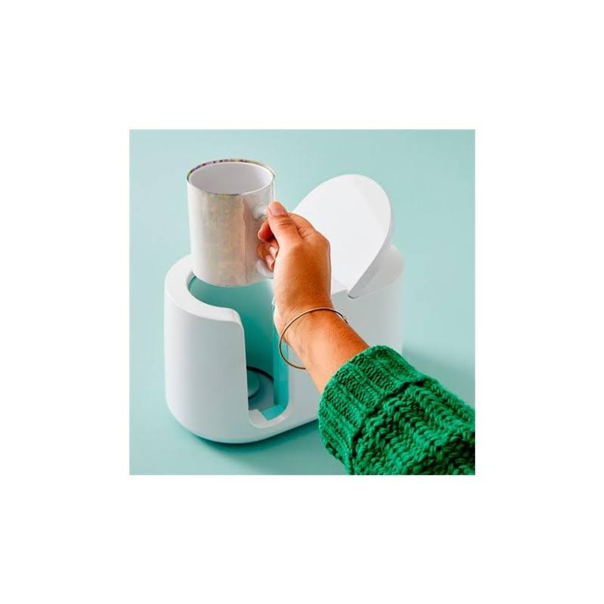 Hand hält eine Tasse in einem weißen Becherwärmer auf hellblauem Hintergrund.