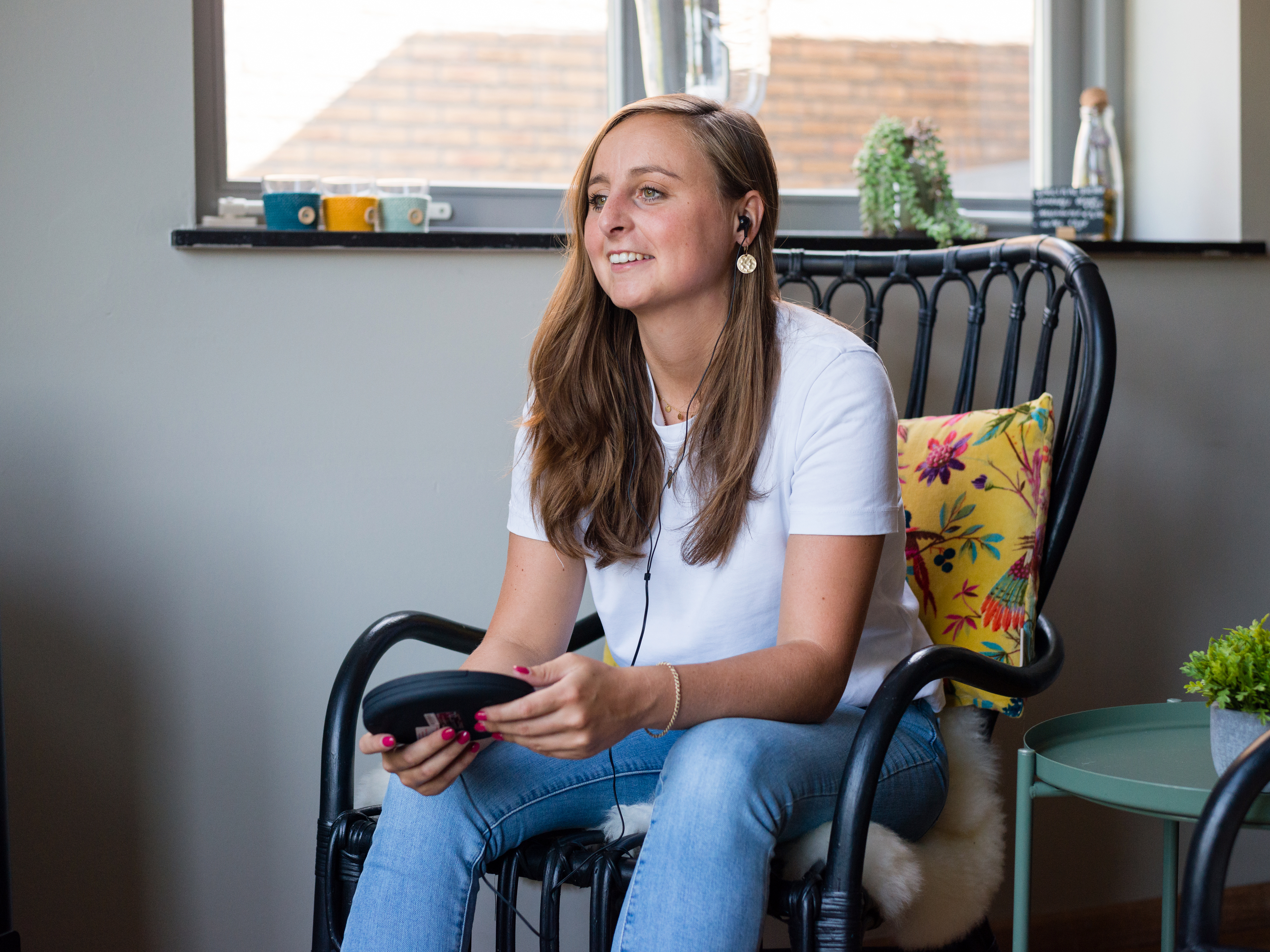 Kobieta w białej koszuli i dżinsach uśmiechnięta, siedząca, w słuchawkach.