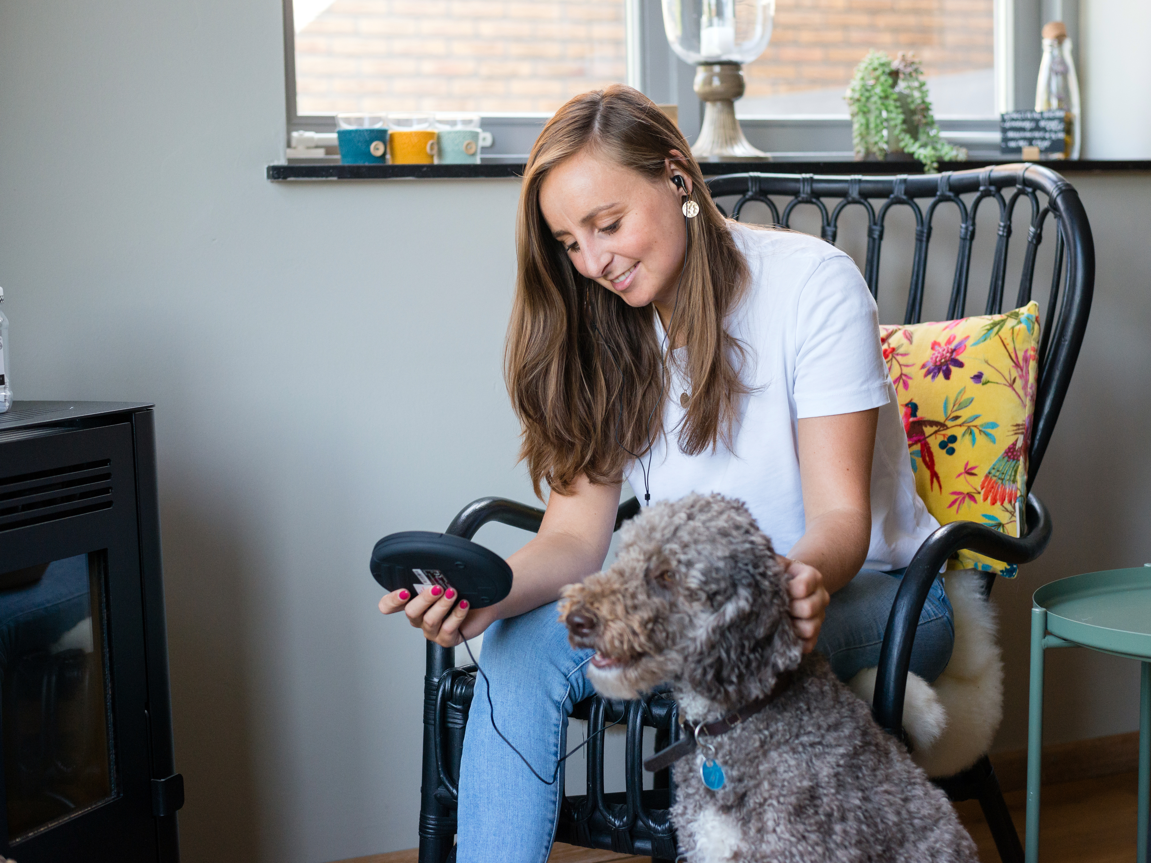 Kobieta siedząca, w słuchawkach, trzymająca urządzenie i głaszcząca psa.
