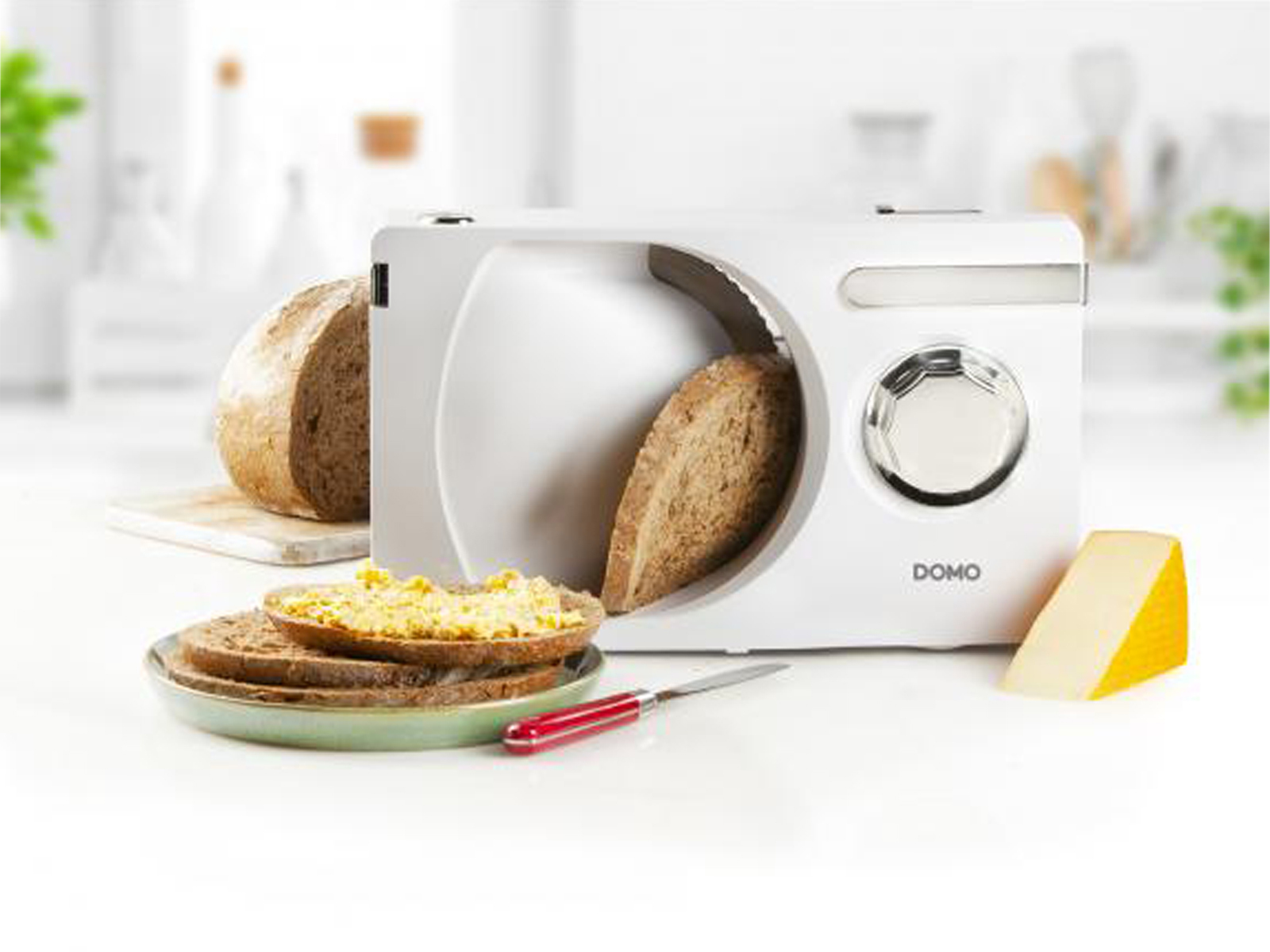 Machine à trancher le pain avec pain, tranches avec tartinade, fromage et couteau sur table.