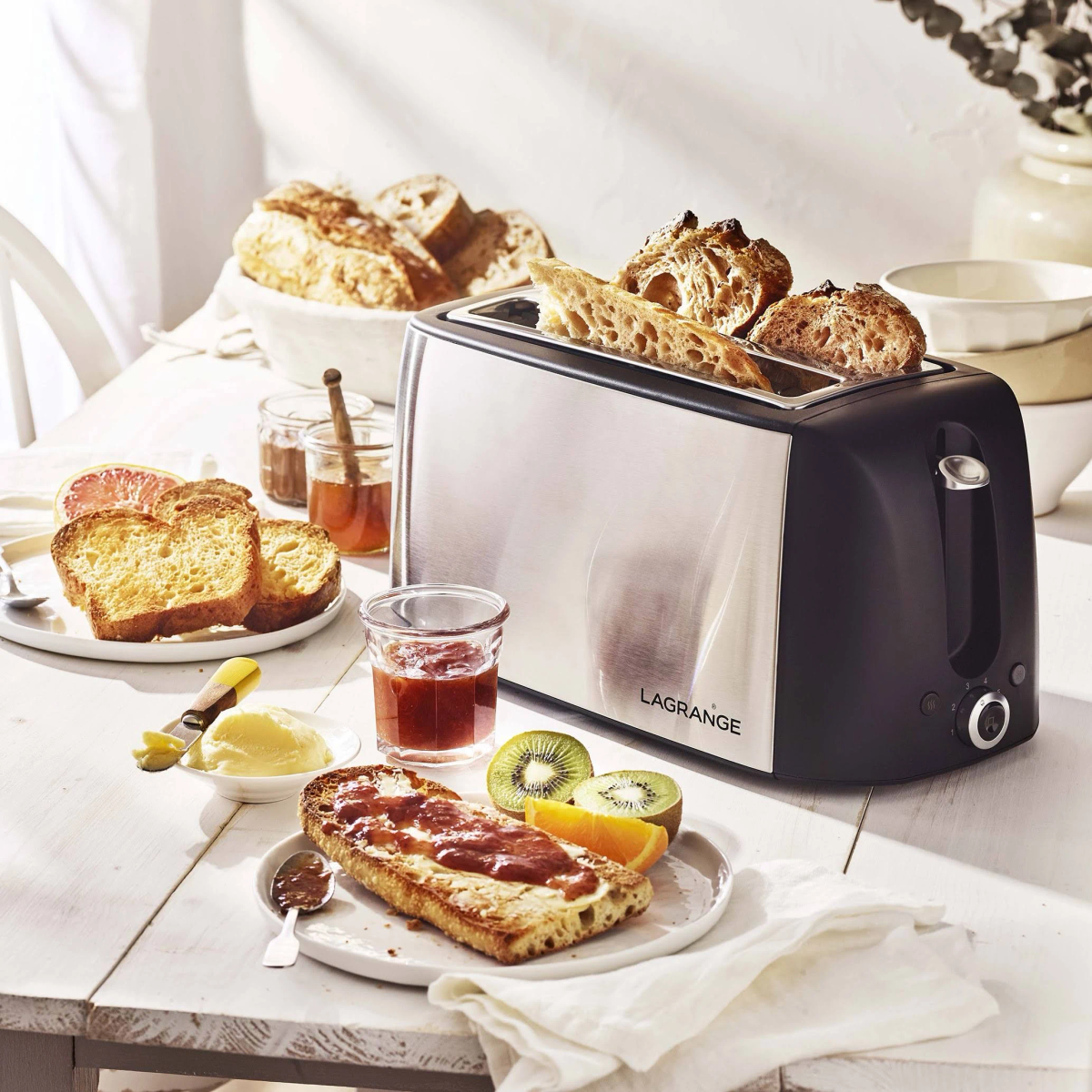 Toaster mit getoastetem Brot. Brot und Marmelade auf dem Tisch mit anderen Lebensmitteln. Weißer Hintergrund.