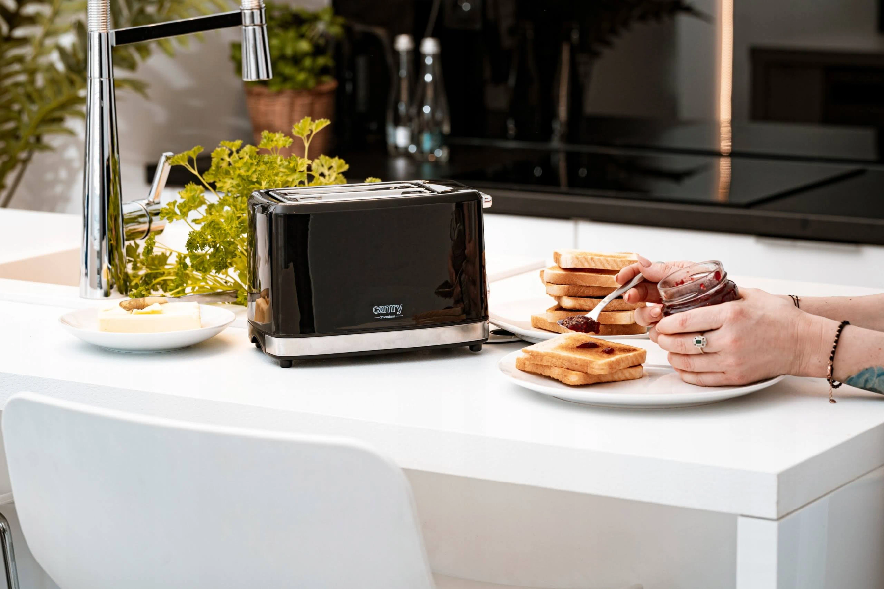 Scena kuchenna z czarnym tosterem i osobą rozsmarowującą dżem na tostach.