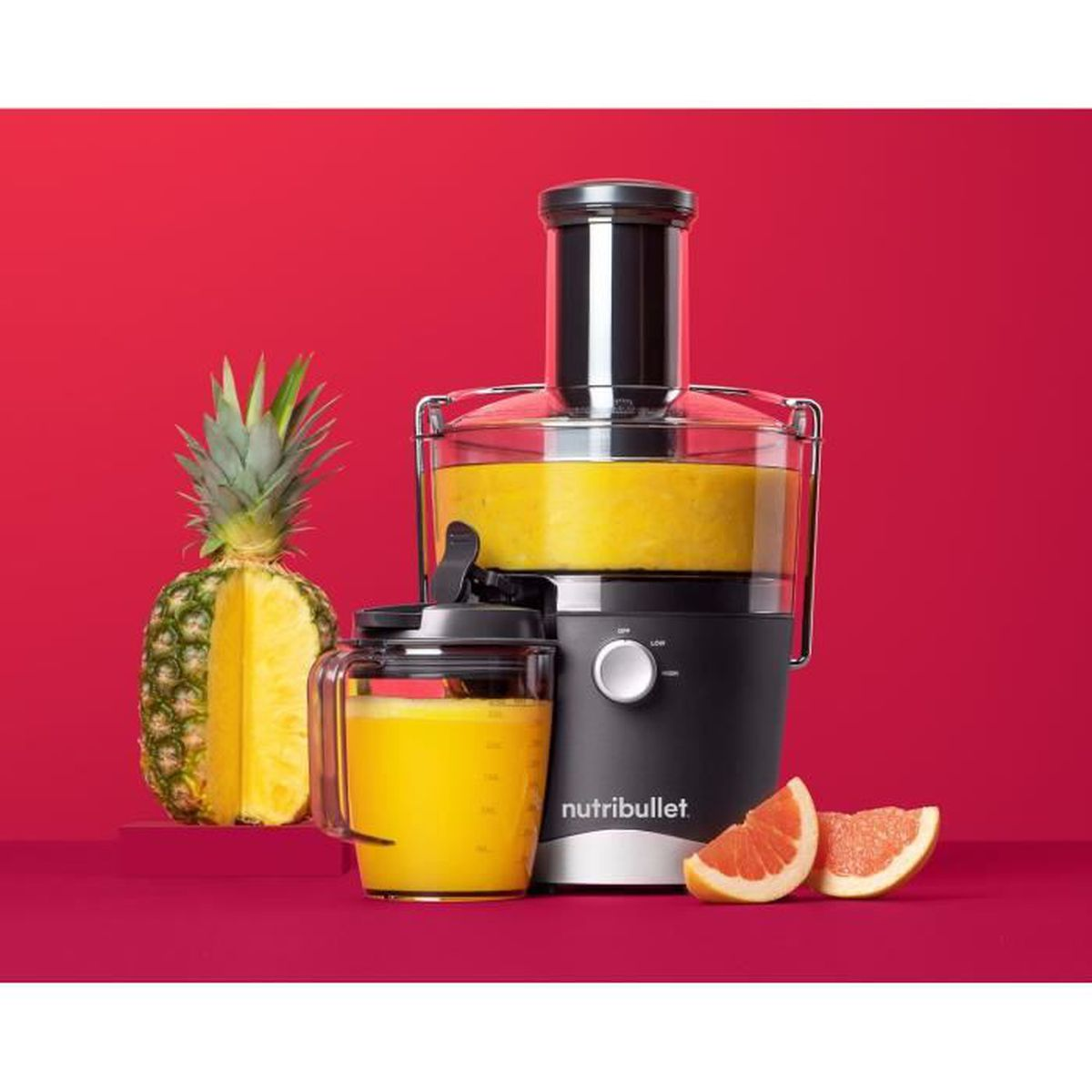 Estrattore di succo con ananas e pompelmo. Succo giallo nel bicchiere e nella caraffa.