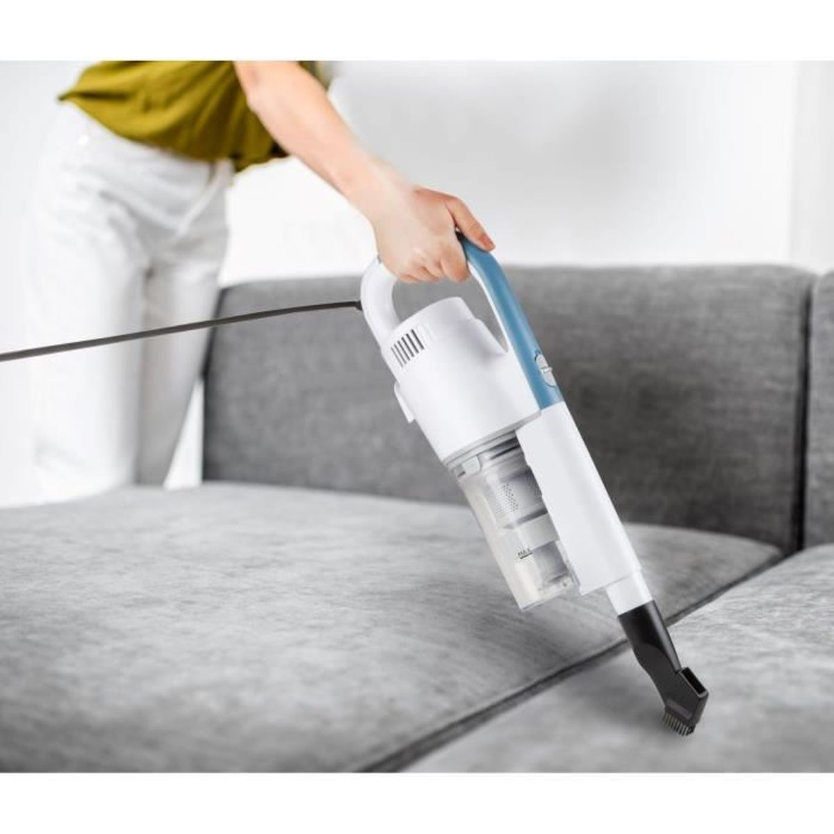 Person verwendet einen Handstaubsauger auf einem grauen Sofa und reinigt die Oberfläche.