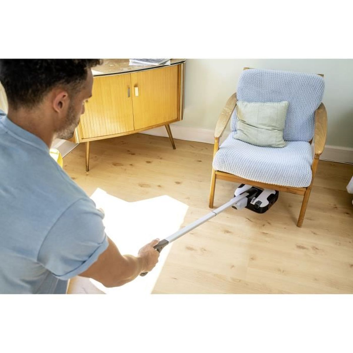 Homme nettoyant un plancher en bois avec une vadrouille. Meubles et chaise visibles en arrière-plan.