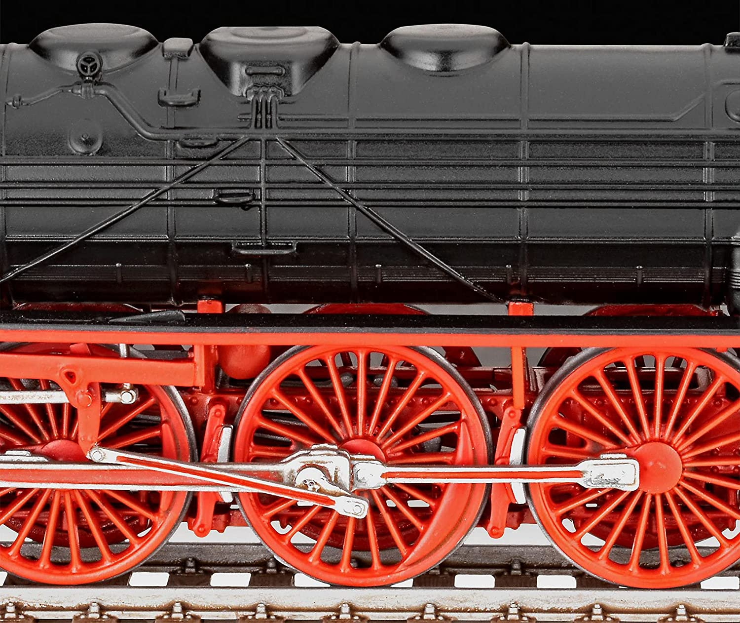 Close-up van een zwart stoomtreinmodel met rode wielen en drijfstangen, op rails.