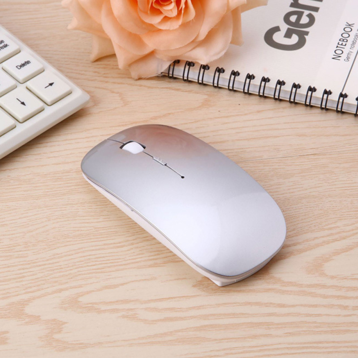 Eine silberne Maus auf einem Holztisch, in der Nähe einer Tastatur und eines Notizblocks, Rose im Hintergrund.