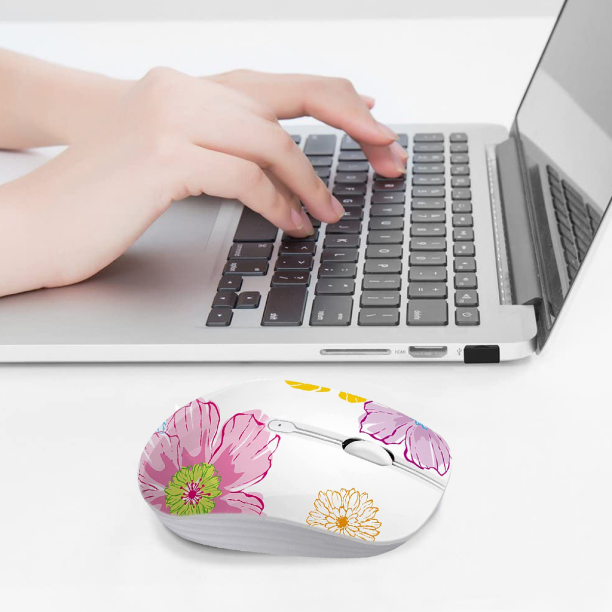 Die Hand einer Person, die eine Blumenausführung einer Maus auf einem Laptop benutzt. Die Maus hat Blumenmuster.