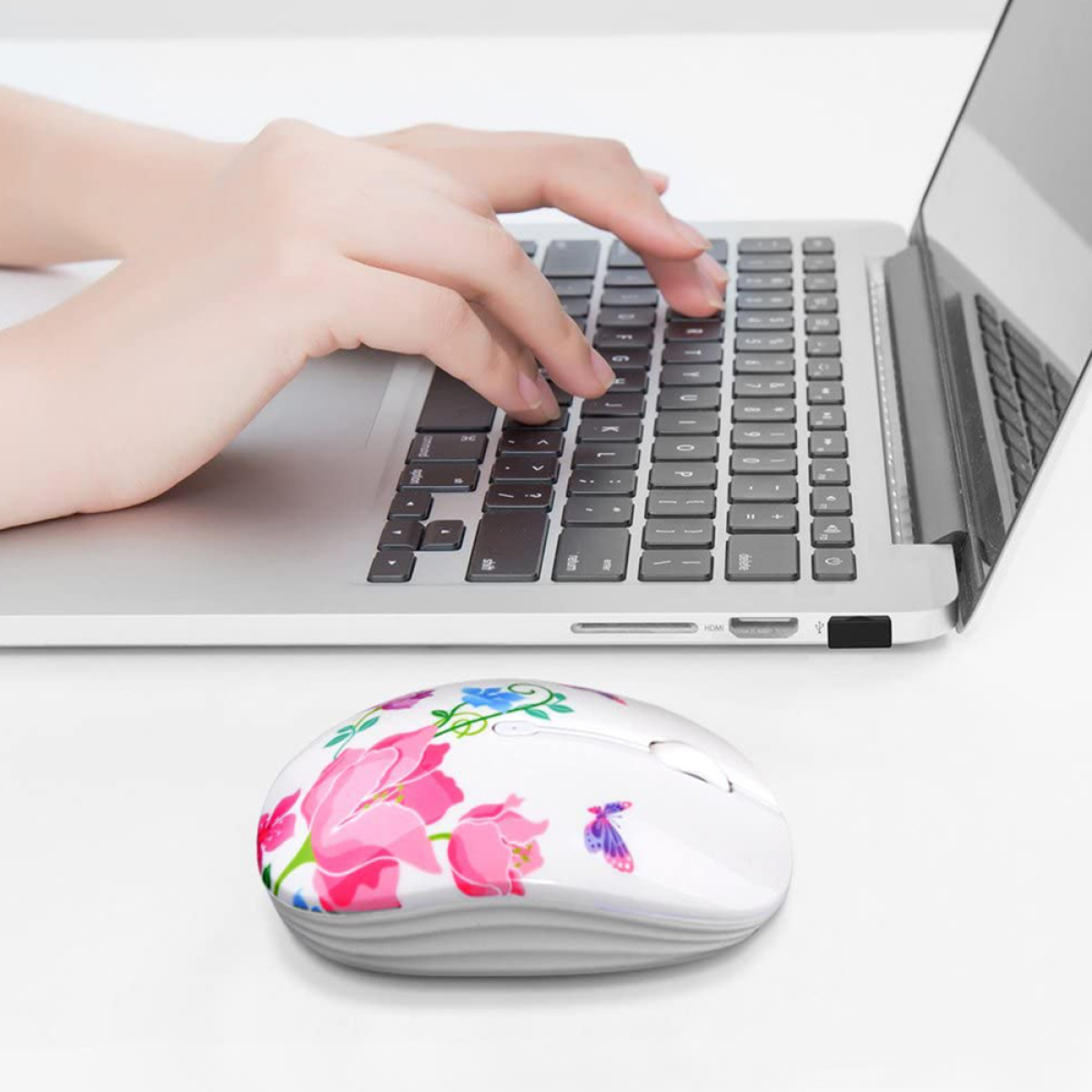 Weiße Maus mit floralem Design, rosa Blumen, neben einem Laptop, Hand tippt.