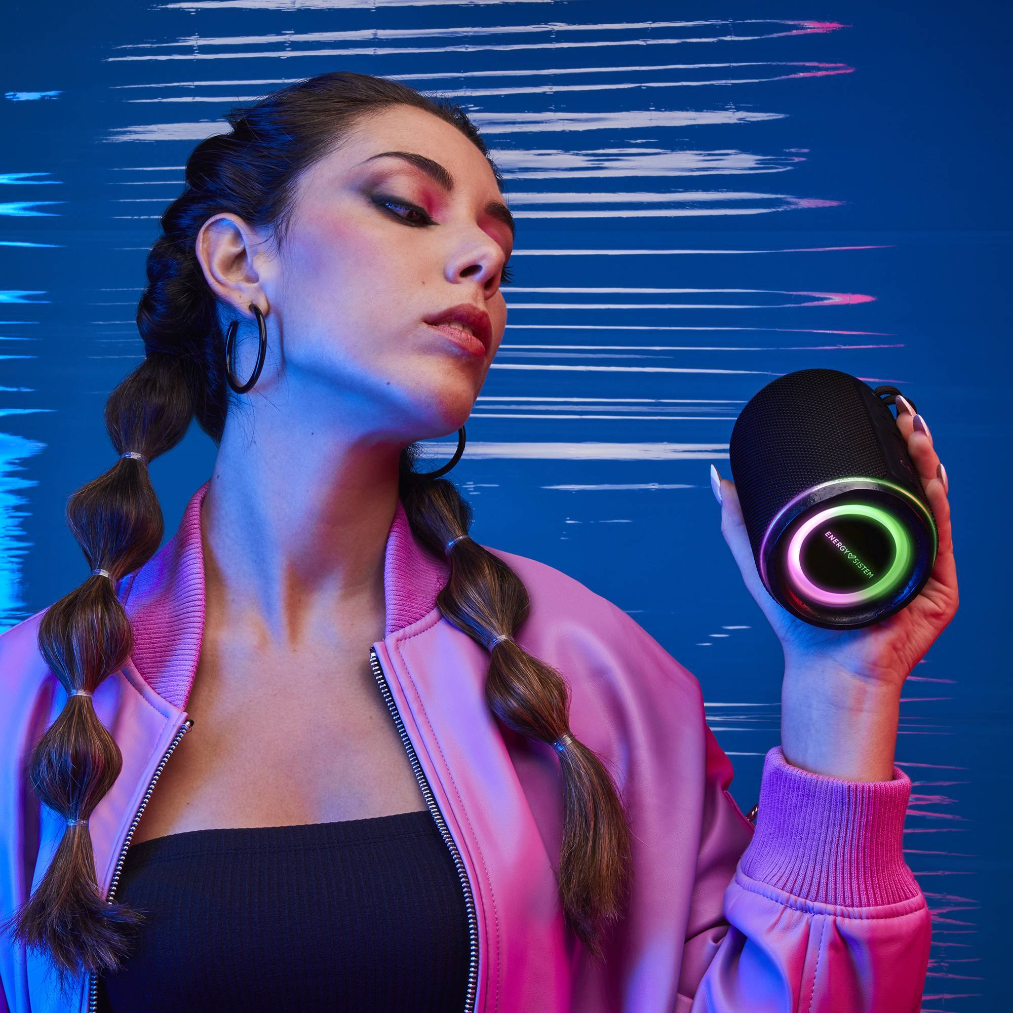 Kobieta trzyma czarny, cylindryczny głośnik ze światłami RGB na niebiesko-białym tle.