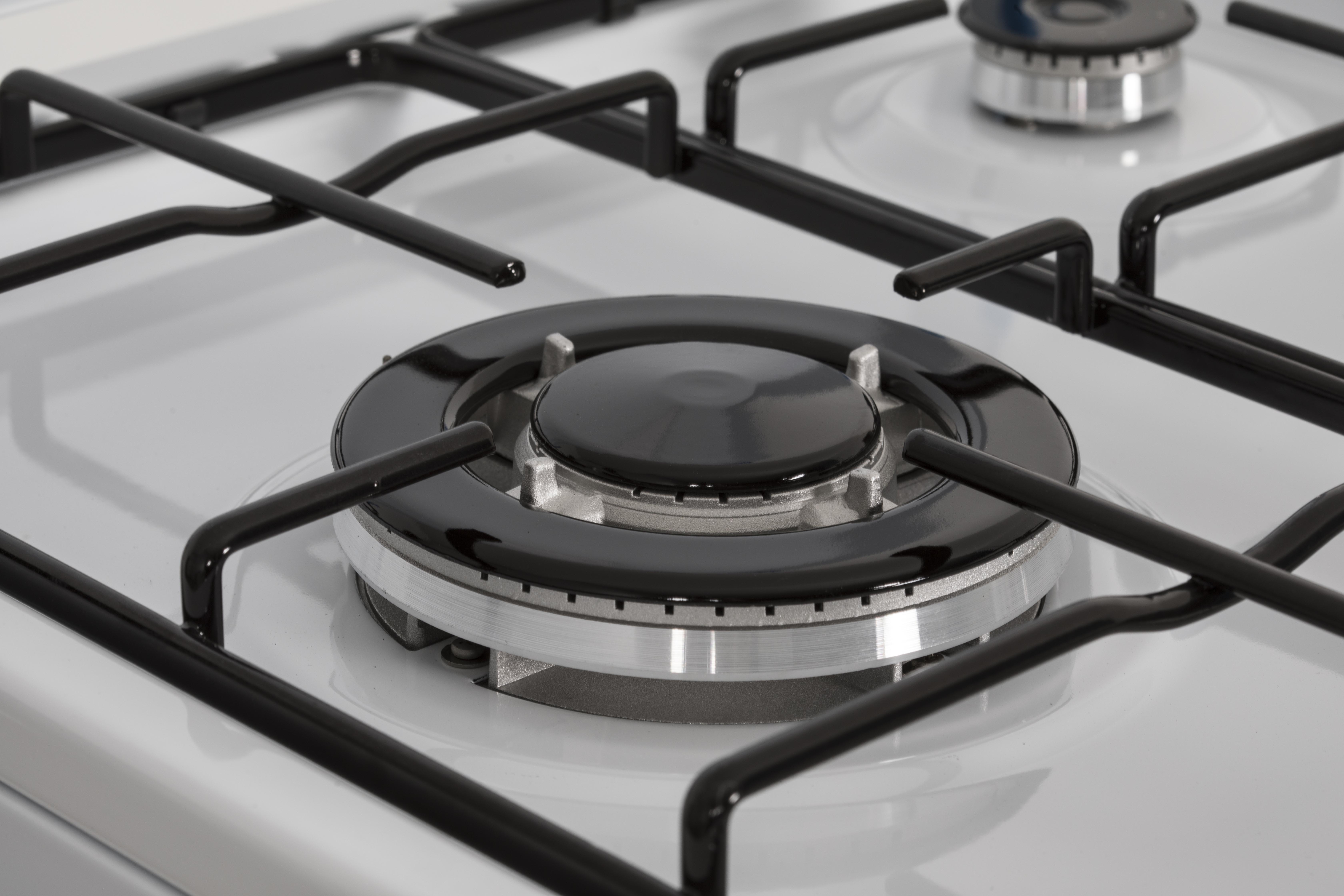 Primer plano de quemadores de cocina de gas. Rejillas y tapas de quemadores negras sobre superficie blanca. Dos quemadores.