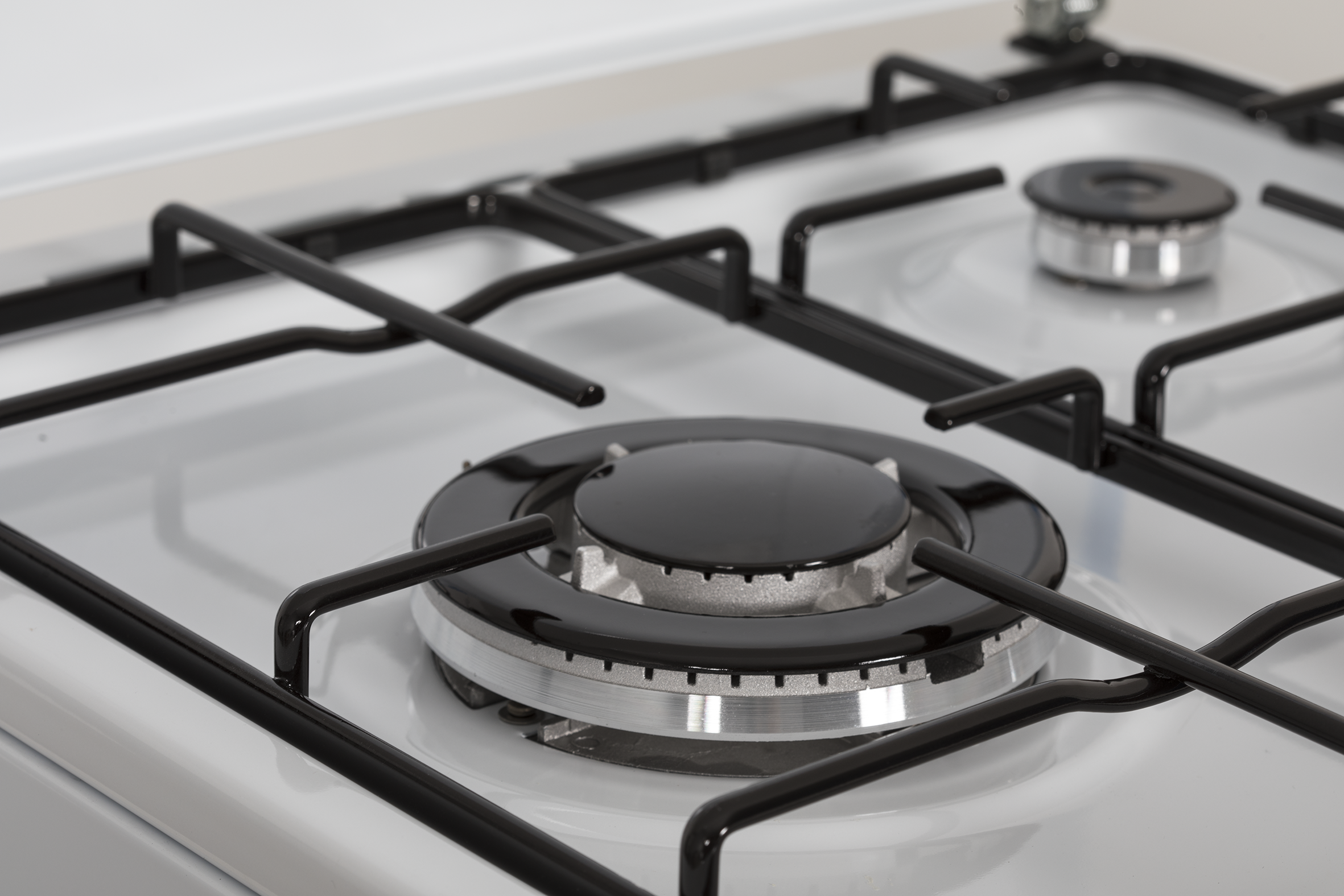 Primer plano de una estufa de gas con parrillas y quemadores negros, aros plateados.