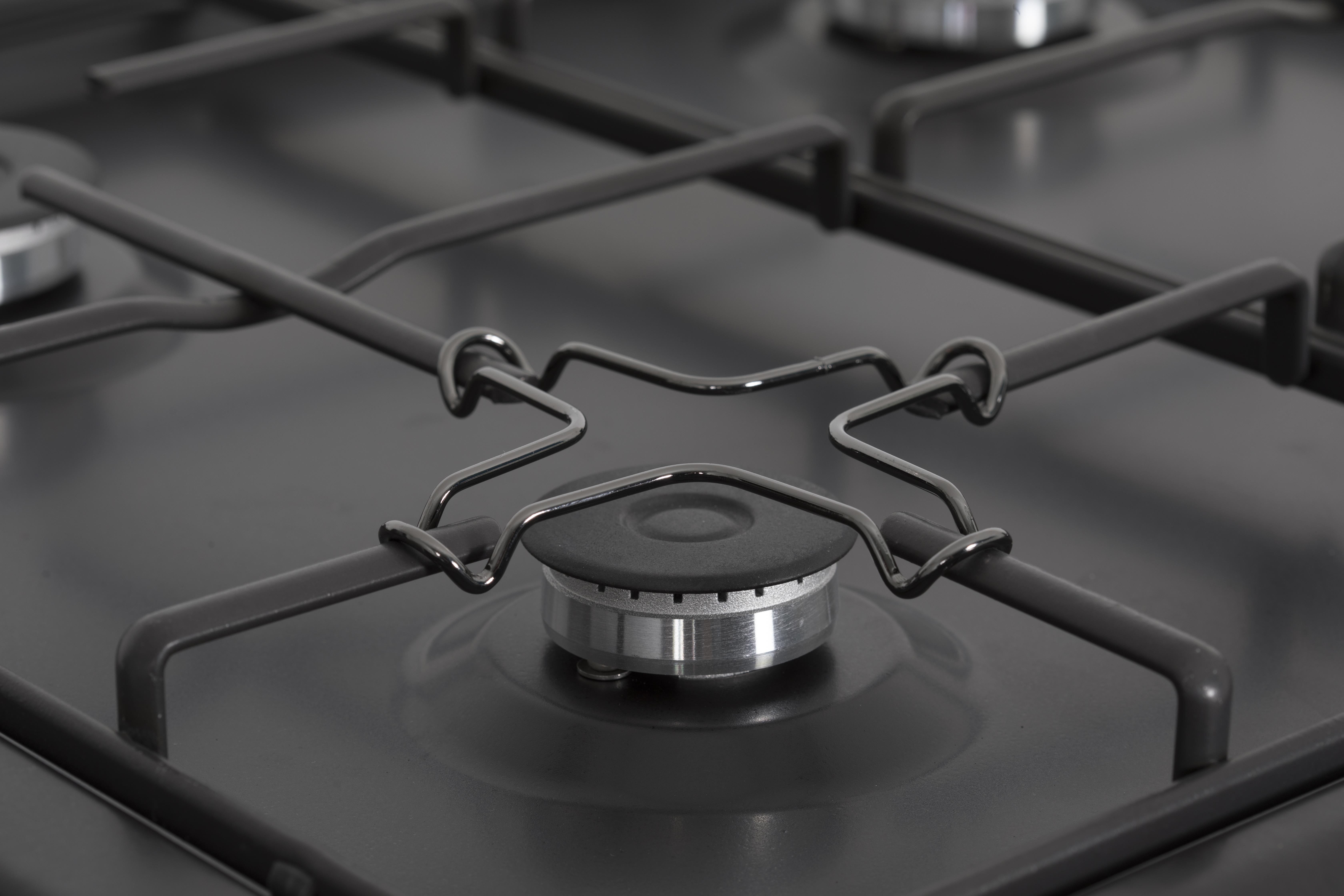 Vista de cerca de una cocina de gas negra con cuatro quemadores y rejillas metálicas.