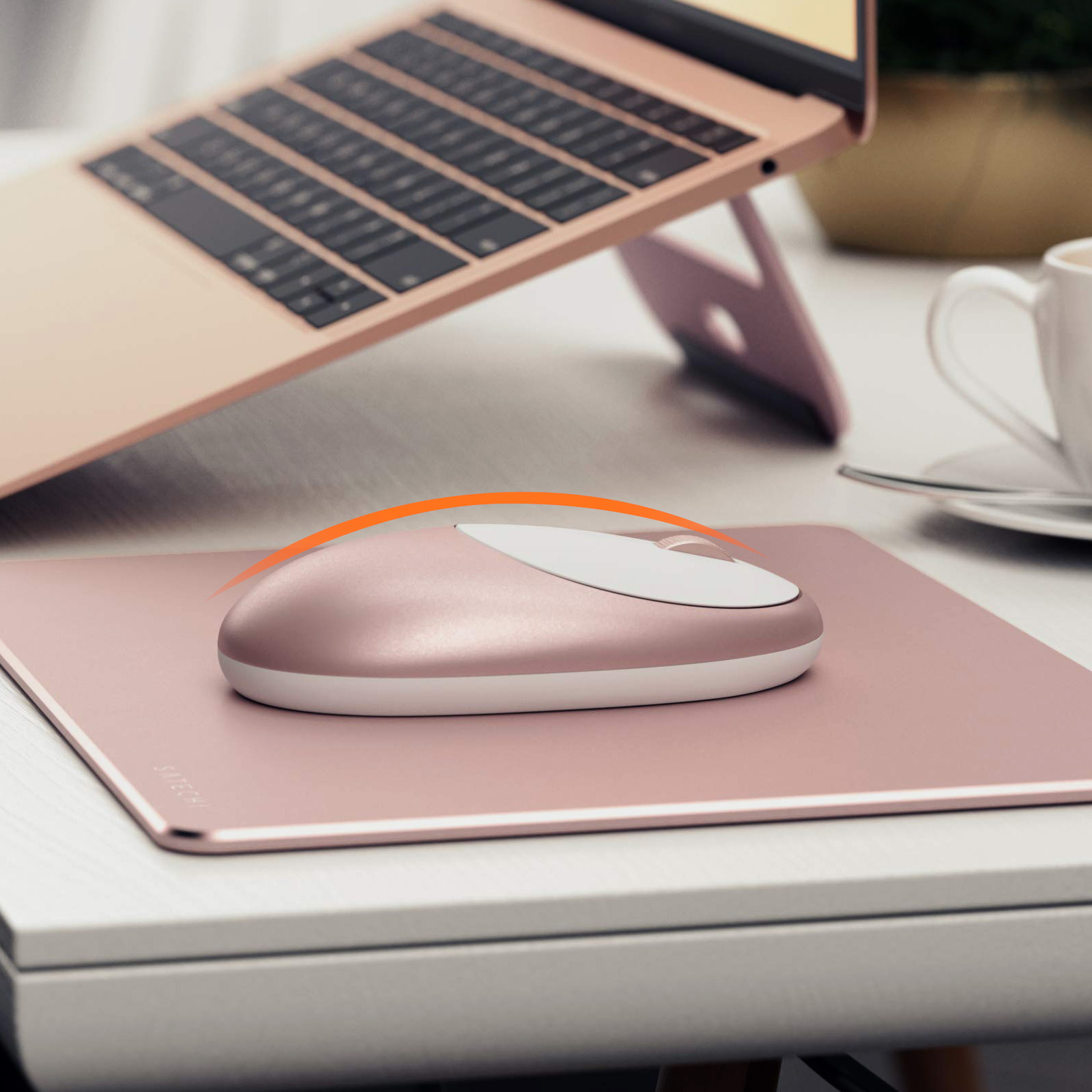 Roze muis op een roze muismat, met een laptop op de achtergrond, op een witte tafel.
