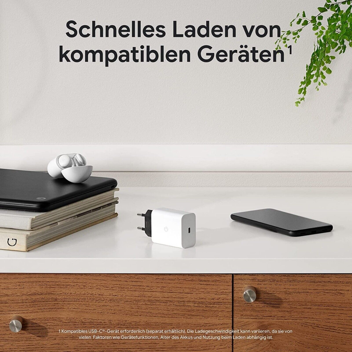 Ein weißes Ladegerät und Kopfhörer auf einem Tisch. Schwarzes Telefon und Bücher sind an der Seite. Grüne Pflanze.