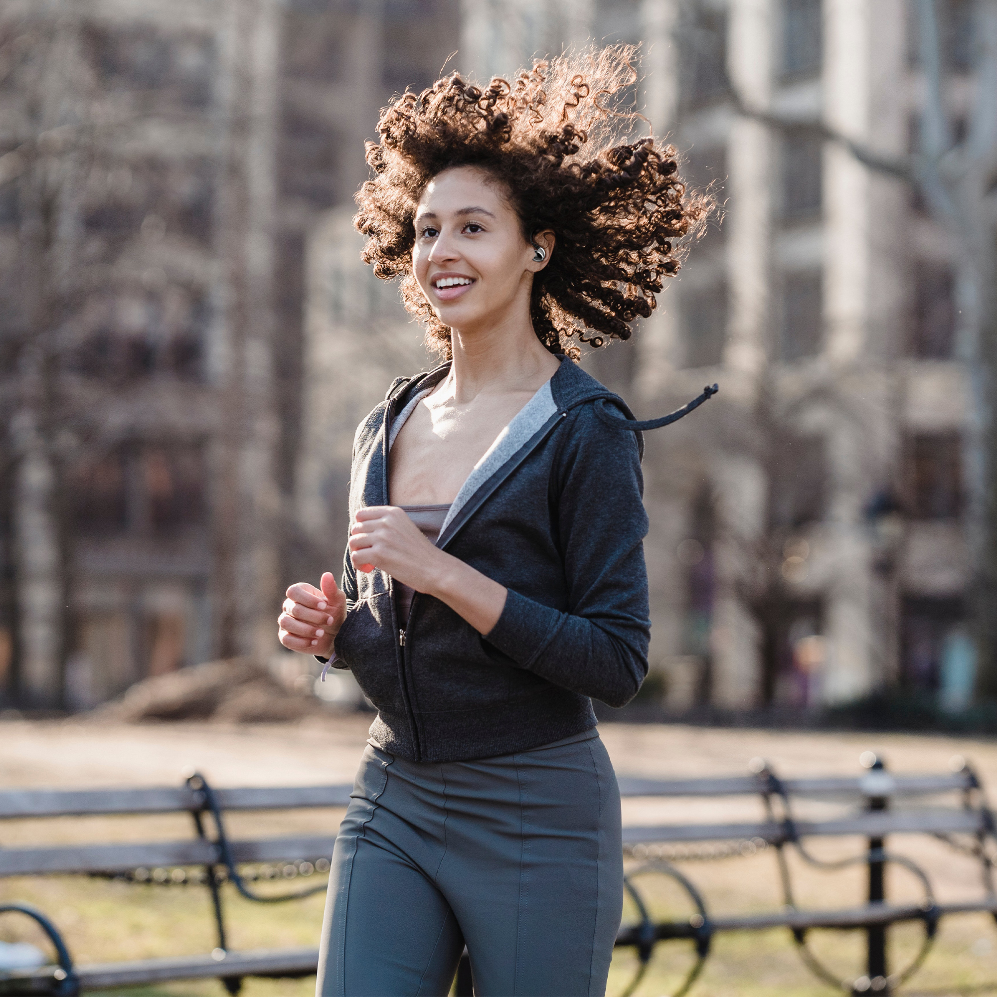 Una giovane donna corre in un parco, con una felpa con cappuccio grigia e leggings, ascoltando musica.
