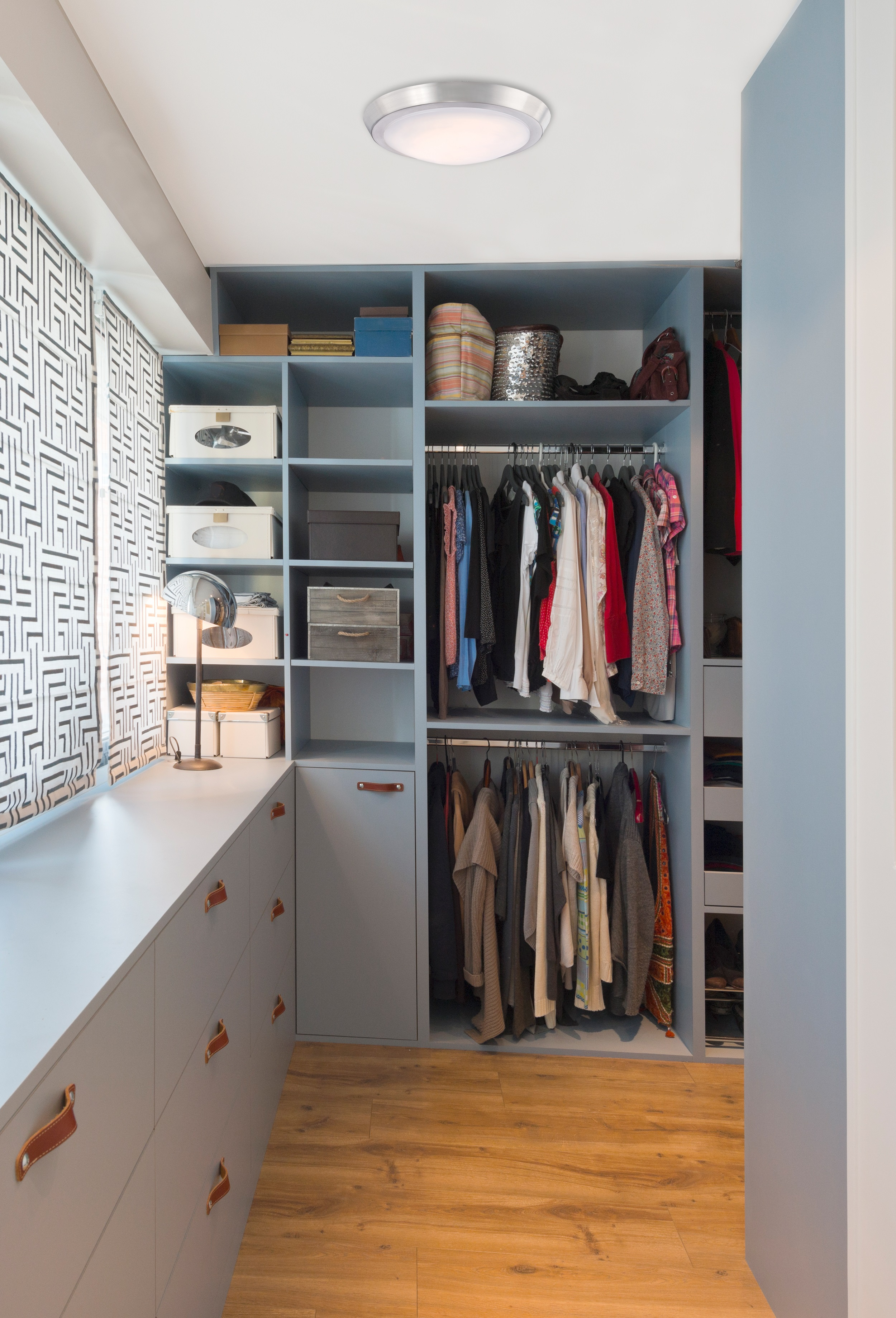 Begehbarer Kleiderschrank mit blauen Wänden und Holzboden. Regale, Schubladen und Kleidung zum Aufhängen sind sichtbar.