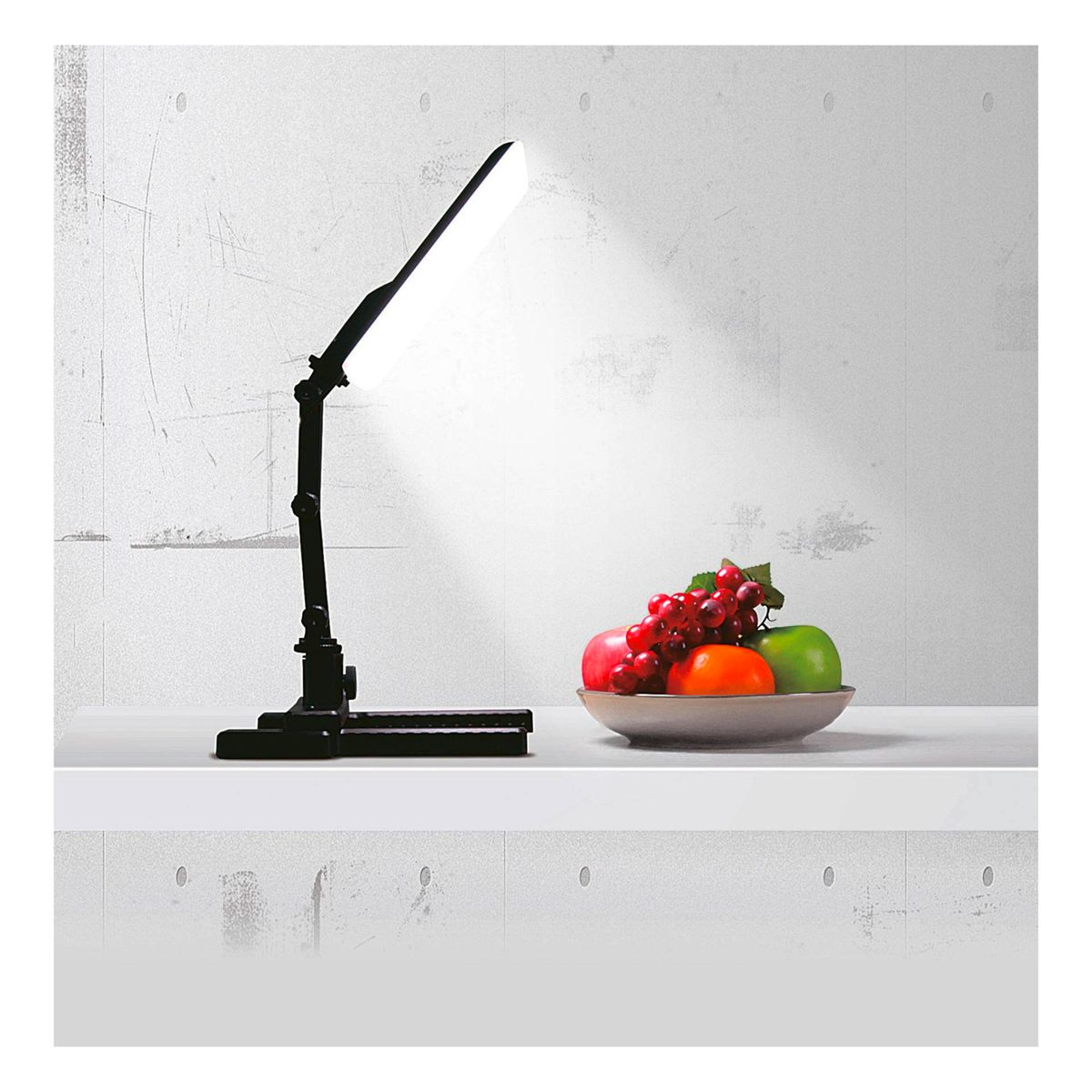 Schwarze Schreibtischlampe beleuchtet eine Obstschale auf weißer Oberfläche.