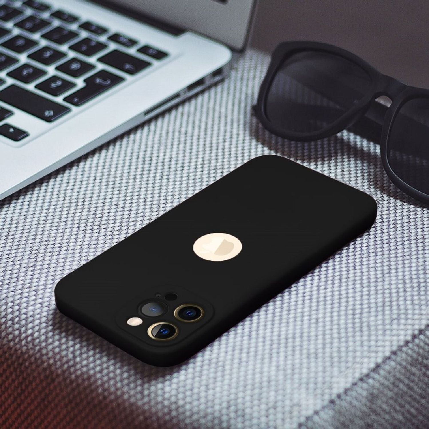 Ein schwarzes Telefon mit Logo, umgeben von einem Laptop und Sonnenbrille auf grauer Oberfläche.