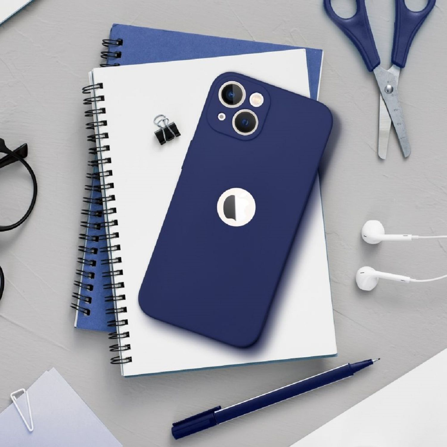 Blaues iPhone auf Notizbüchern mit Schere und Kopfhörern auf grauer Fläche.