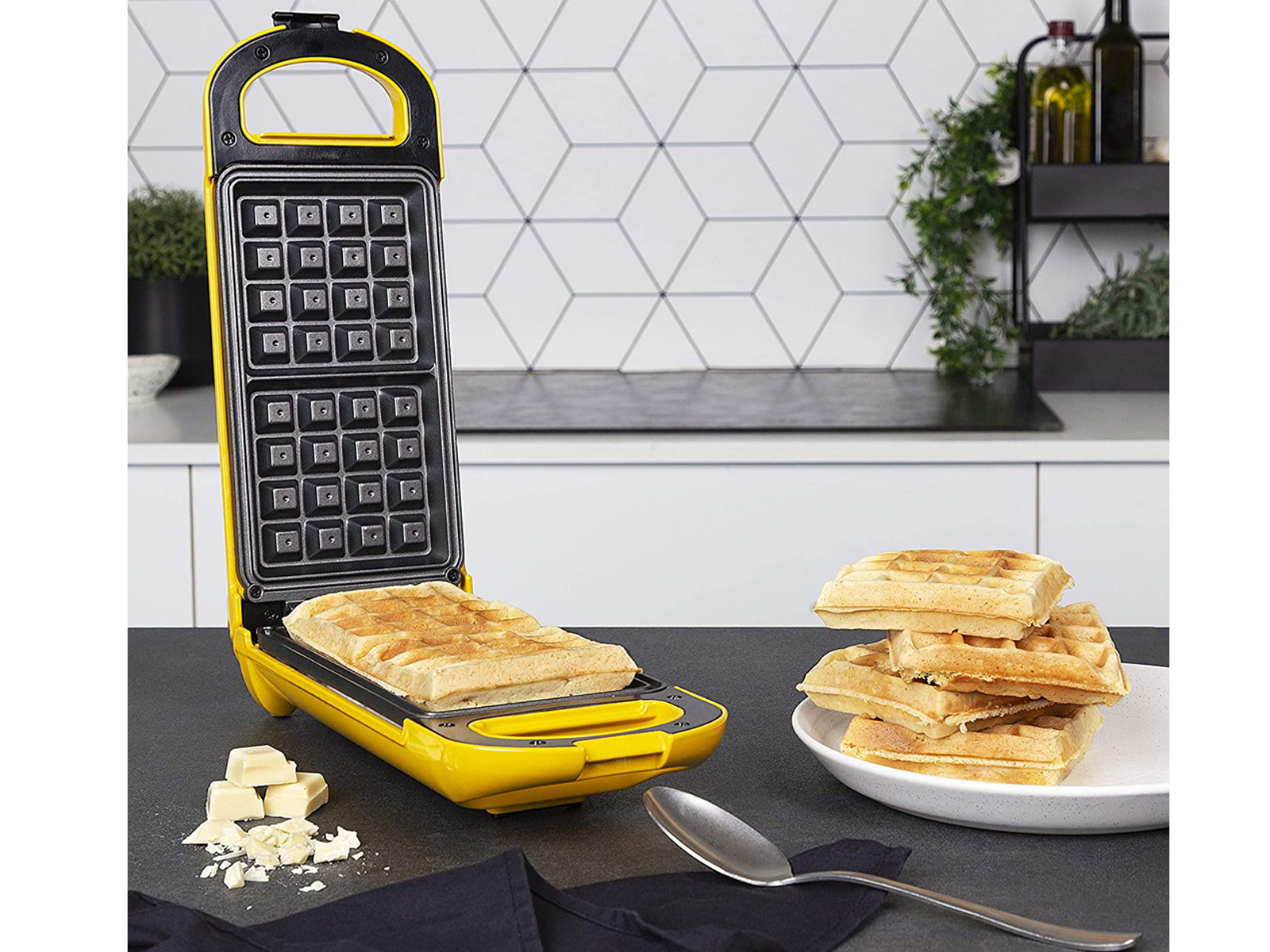 Waffle maker con waffle. Waffle maker giallo con waffle in cottura e impilati. Cioccolato bianco.