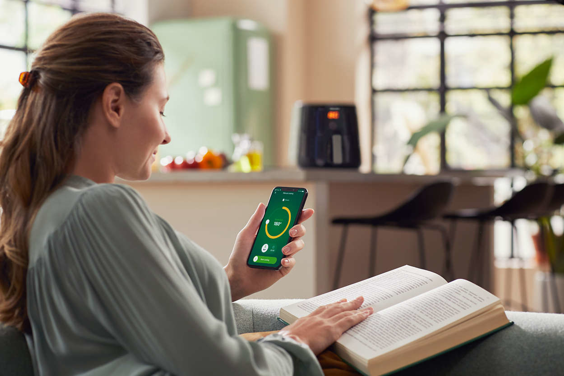 Kobieta używa telefonu, przeglądając aplikację z frytkownicą w tle.