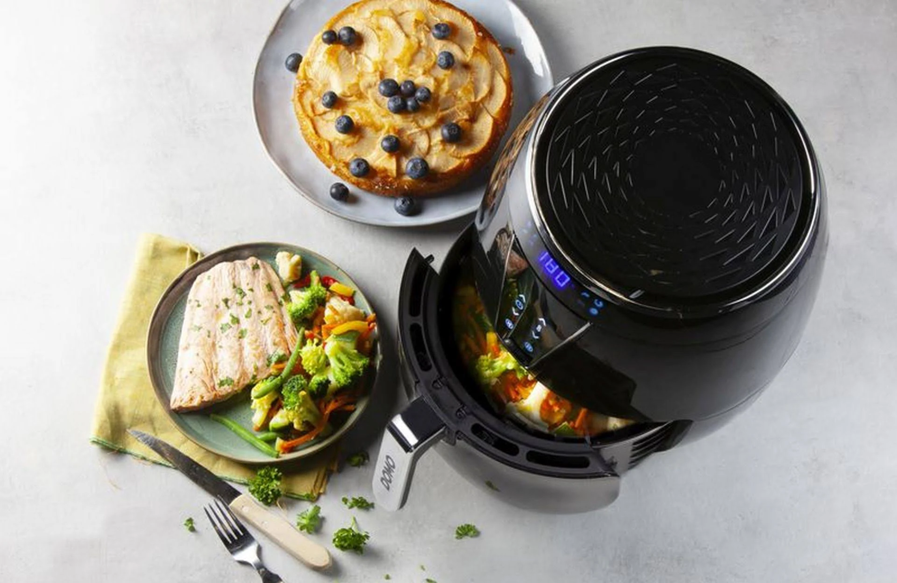 Otwarta frytkownica beztłuszczowa z jedzeniem. Dania na stole. Biała powierzchnia.