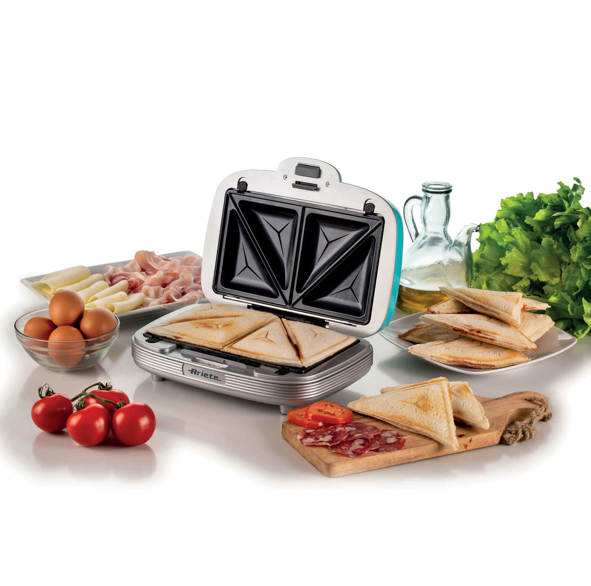 Otwarta opiekacza do kanapek z kanapkami w środku. Składniki takie jak pomidory, jajka i ser w pobliżu.