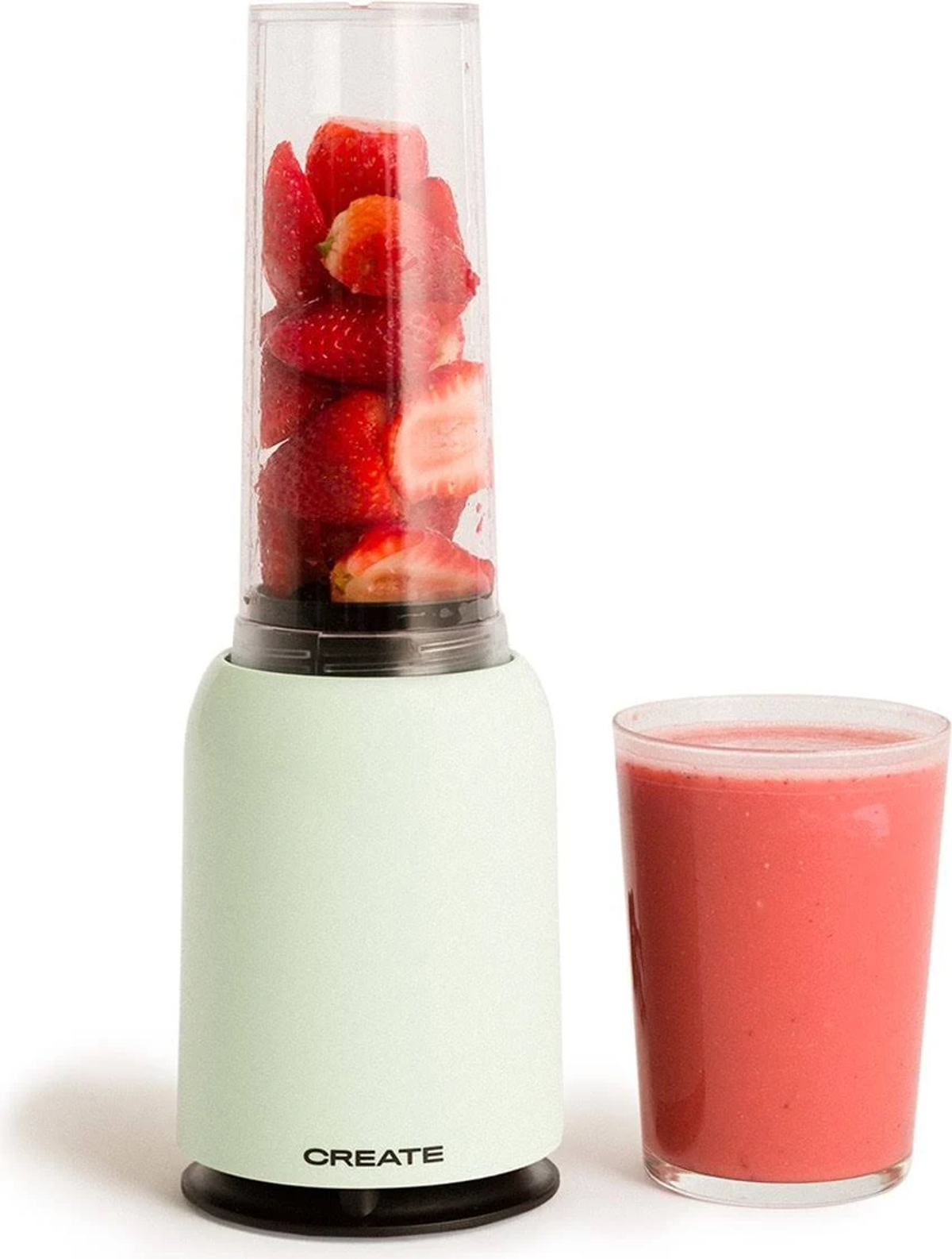 Una licuadora con fresas y un vaso de batido rosa sobre blanco.