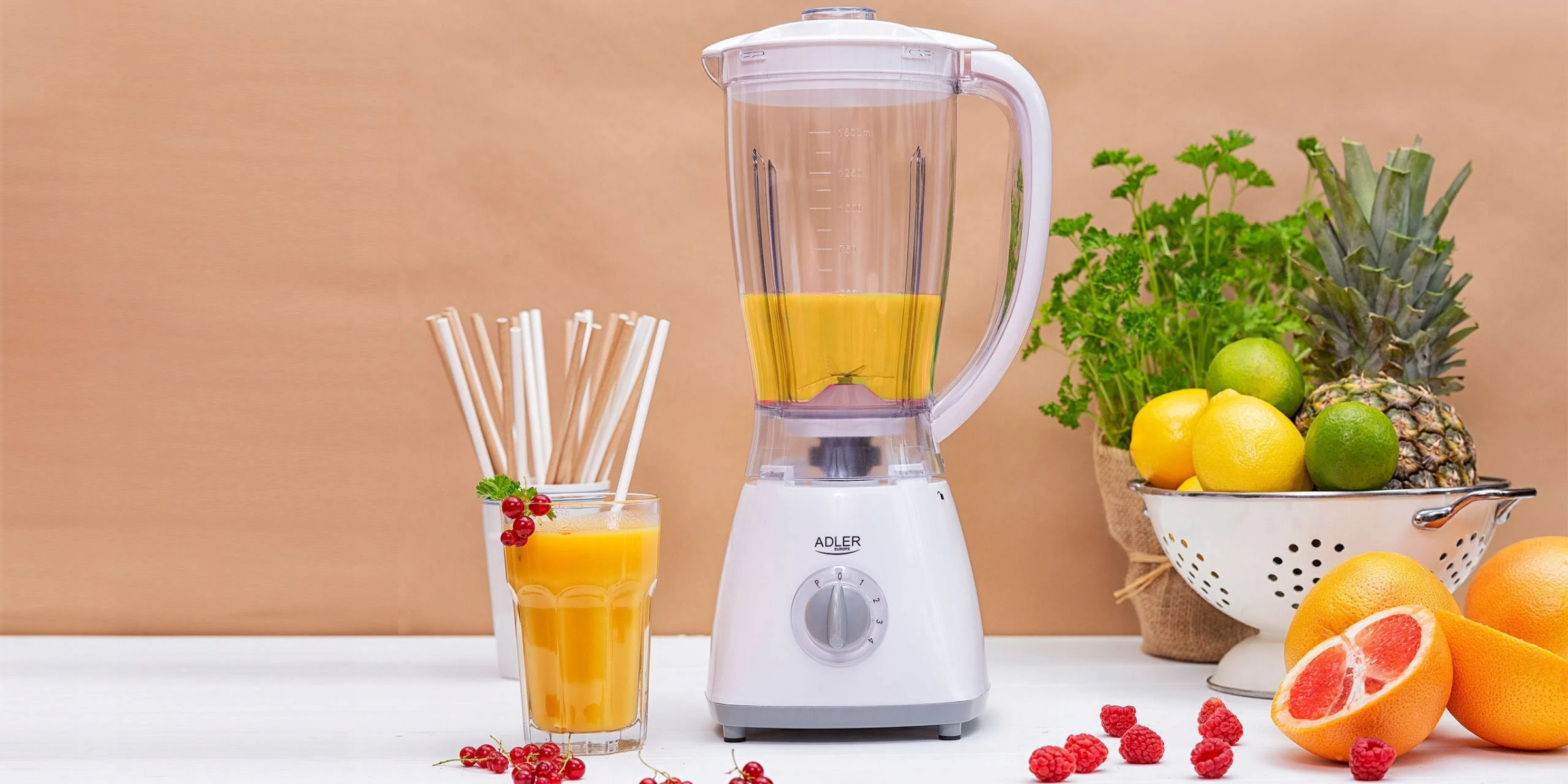 Biały blender z sokiem pomarańczowym, szklanką i owocami takimi jak ananas, pomarańcze i cytryny.