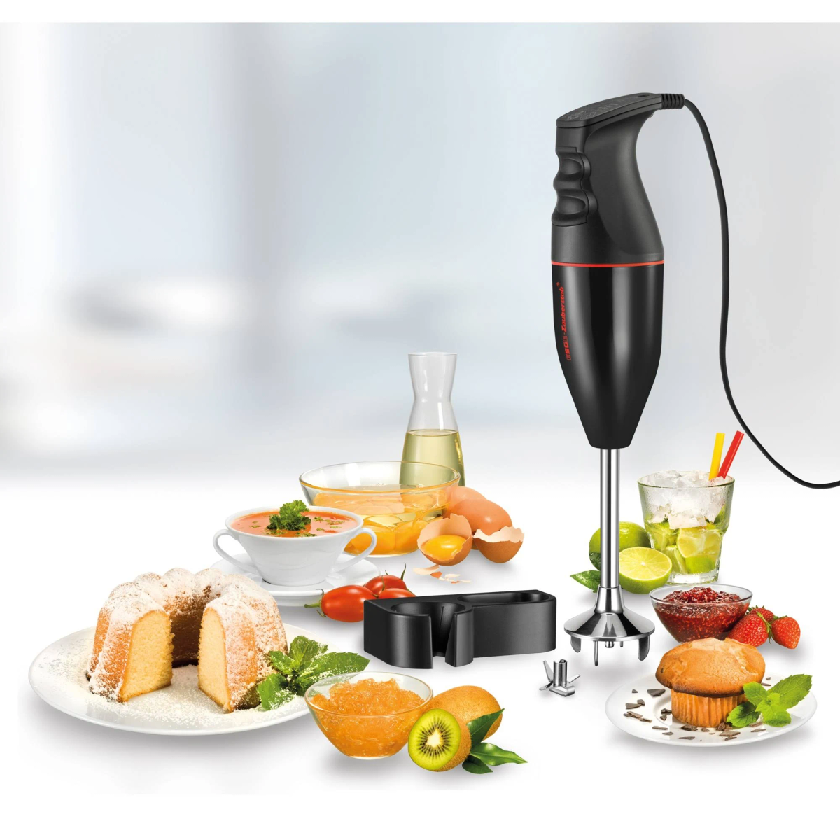 Zwarte staafmixer met accessoires en bereide gerechten op een tafel.