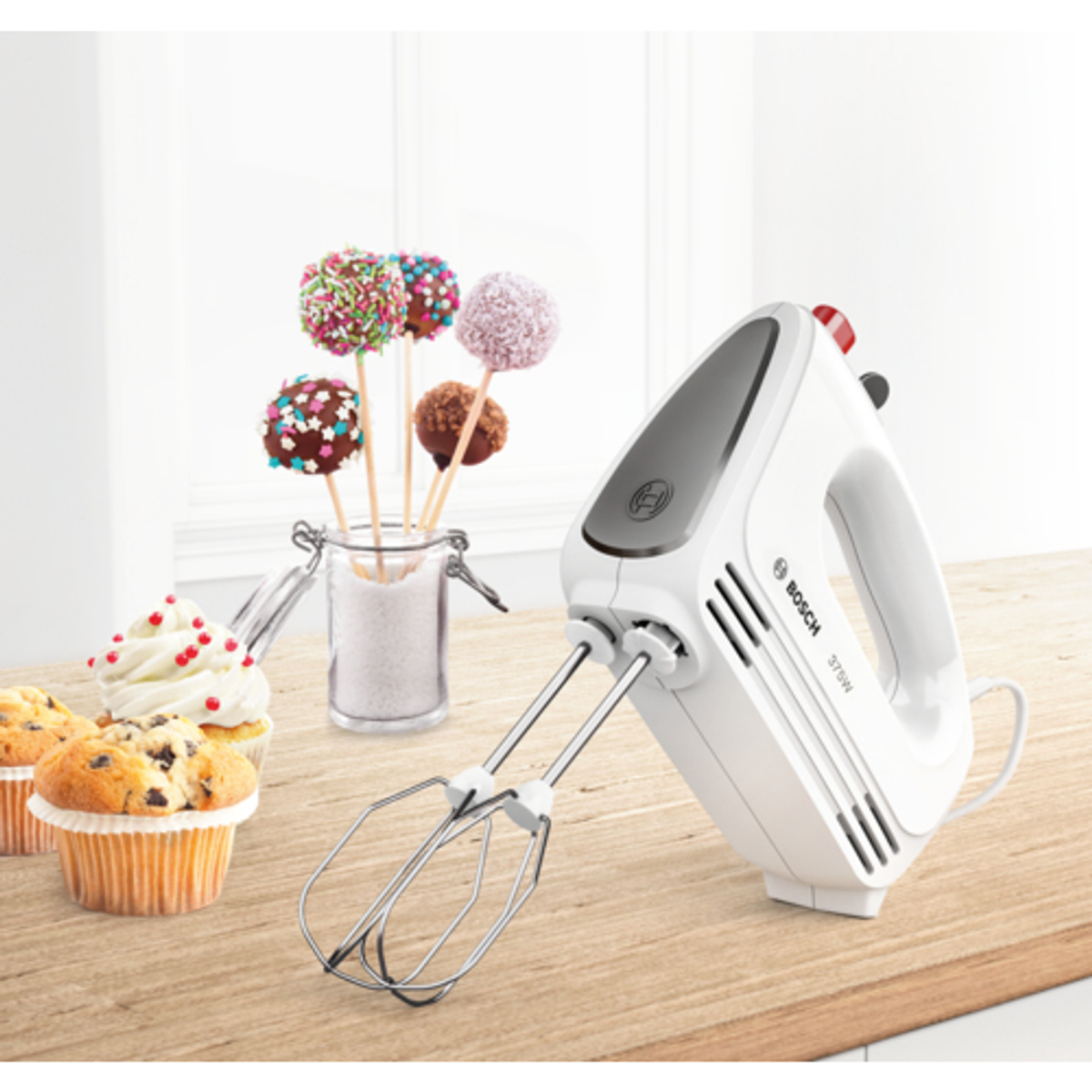 Frullatore a mano bianco con cupcake e cake pop. Tavolo in legno con sfondo chiaro.