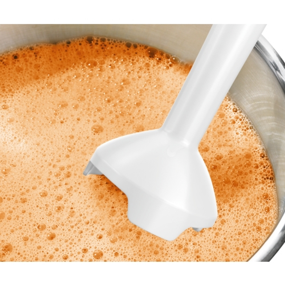 Biały blender ręczny w misce. Zmieszany płyn jest pomarańczowy. Misa ze stali nierdzewnej.