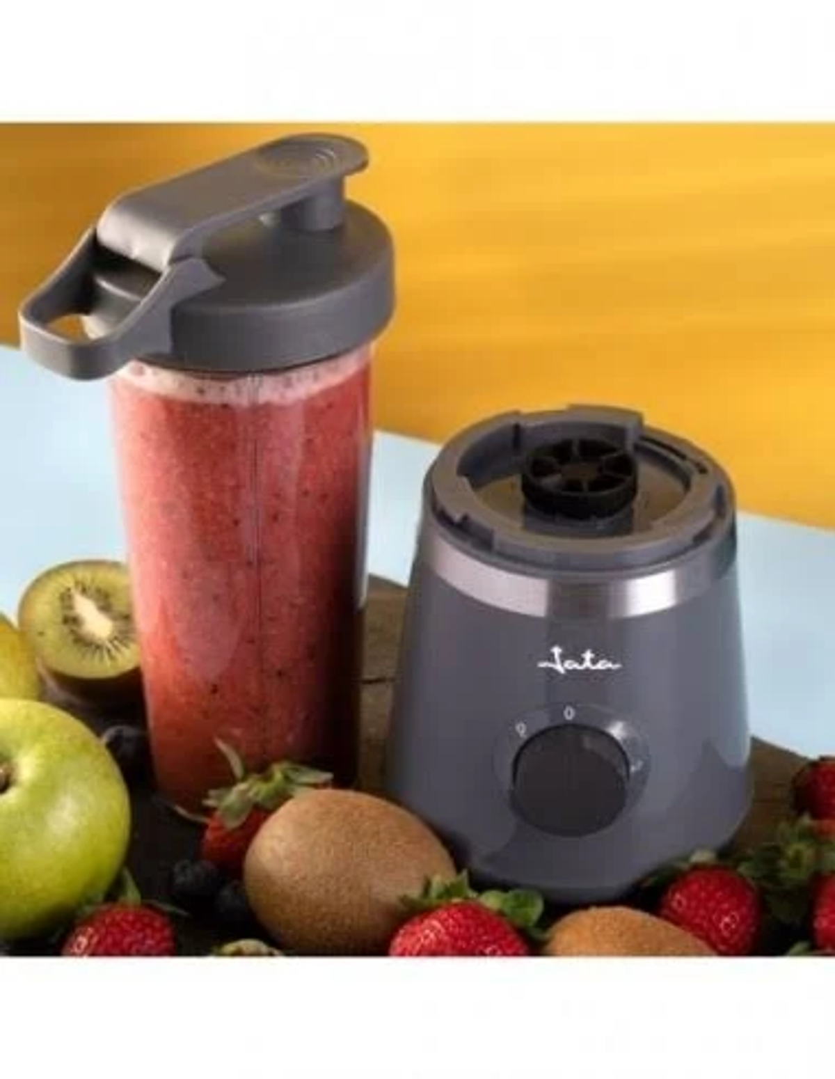 Frullatore grigio con un frullato. Il frullatore ha un manico ed è circondato dalla frutta.
