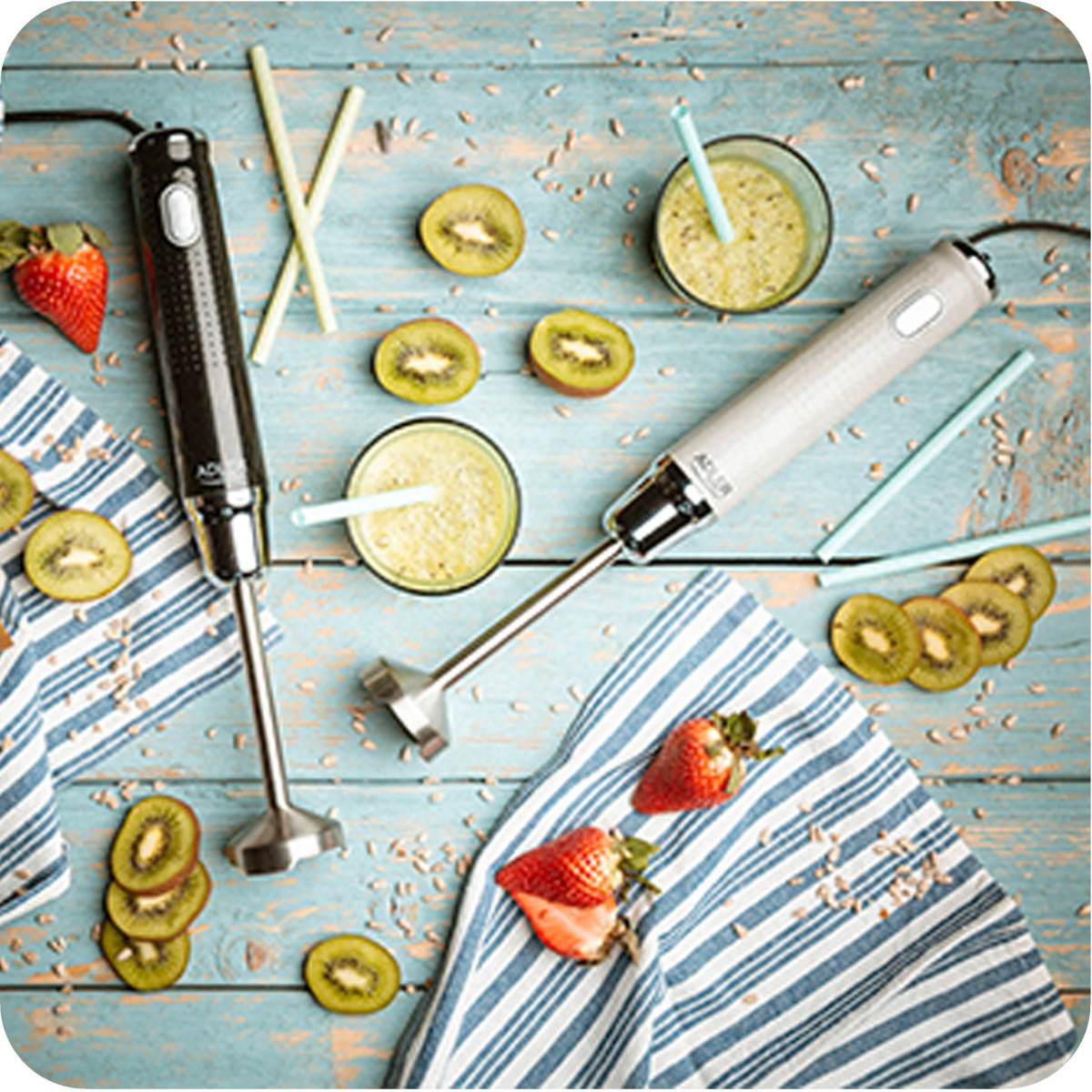 Dwa blendery ręczne na niebieskiej drewnianej powierzchni z owocami i napojami, tworząc orzeźwiającą scenę.