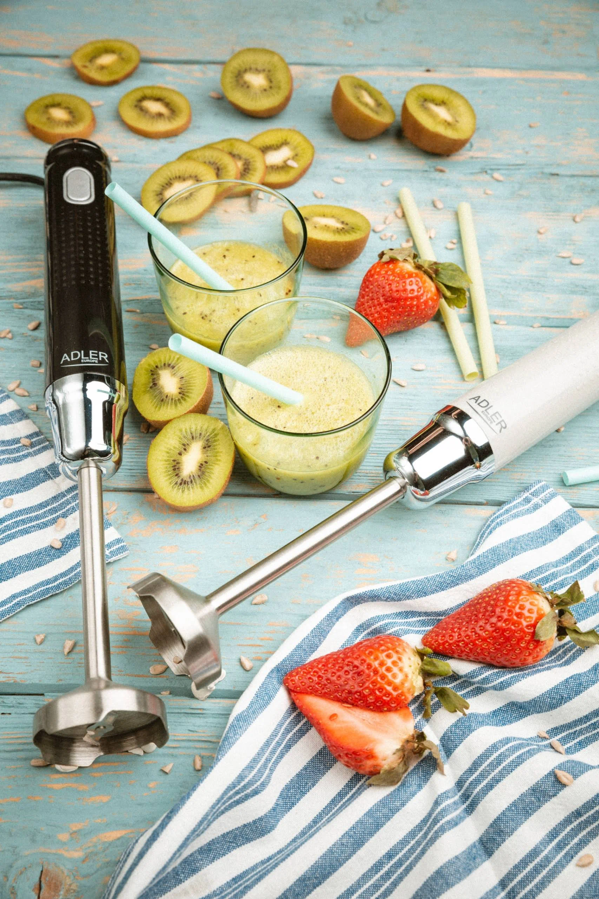 Dwa blendery ze smoothie i plasterkami kiwi z truskawkami na drewnianym stole.