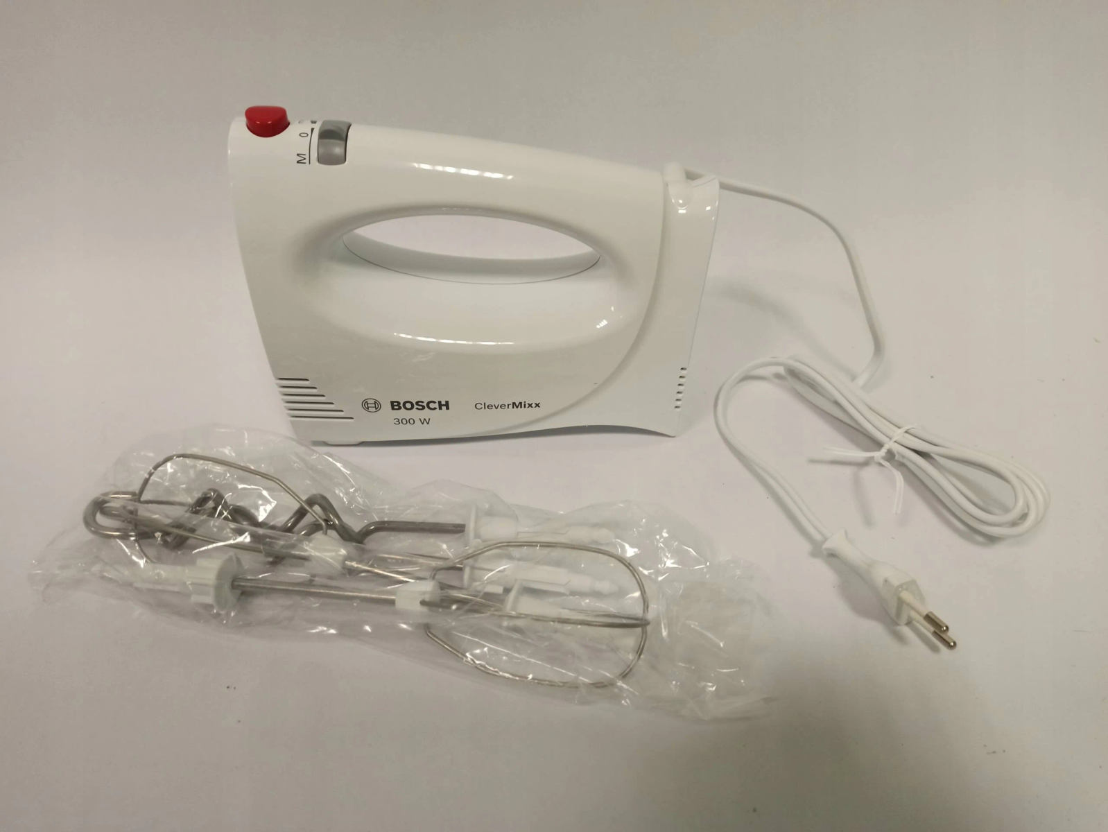 A white hand mixer with attachments and a power cord on a white surface.