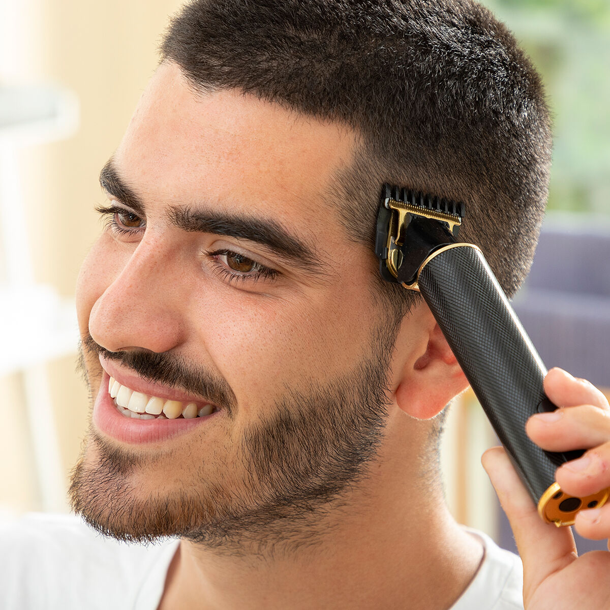 Lächelnder Mann, der einen schwarz-goldenen Haarschneider benutzt, um seine Haare zu schneiden.