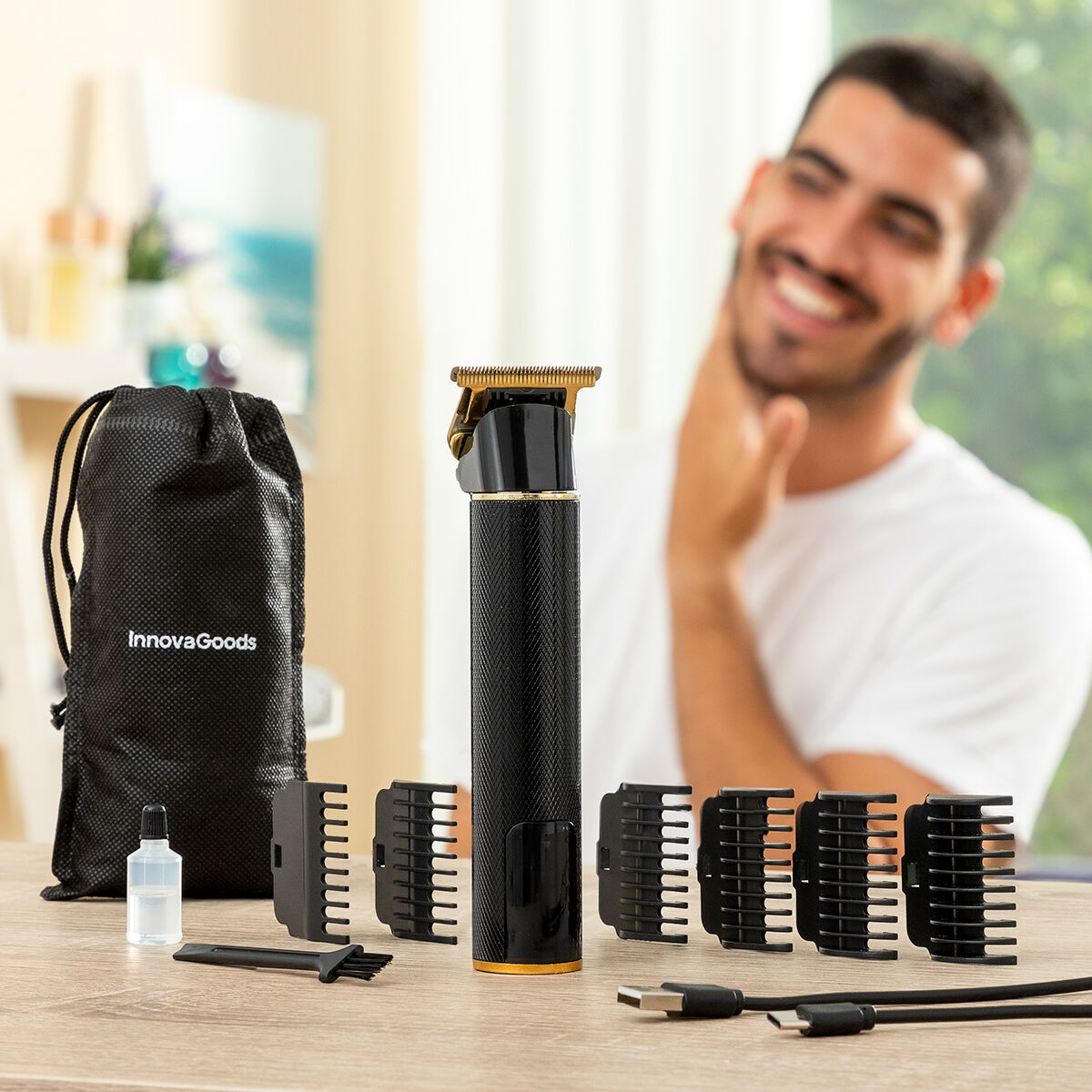 Mann lächelt hinter einem Tisch mit Haarschneider, Zubehör und einer schwarzen InnovaGoods-Tasche.