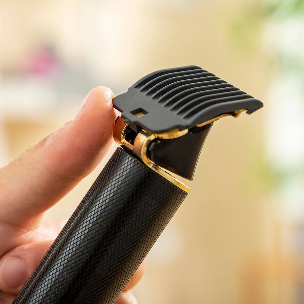 Ein schwarzer Haarschneider mit goldenen Akzenten und einem Kammaufsatz. Von einer Hand gehalten.