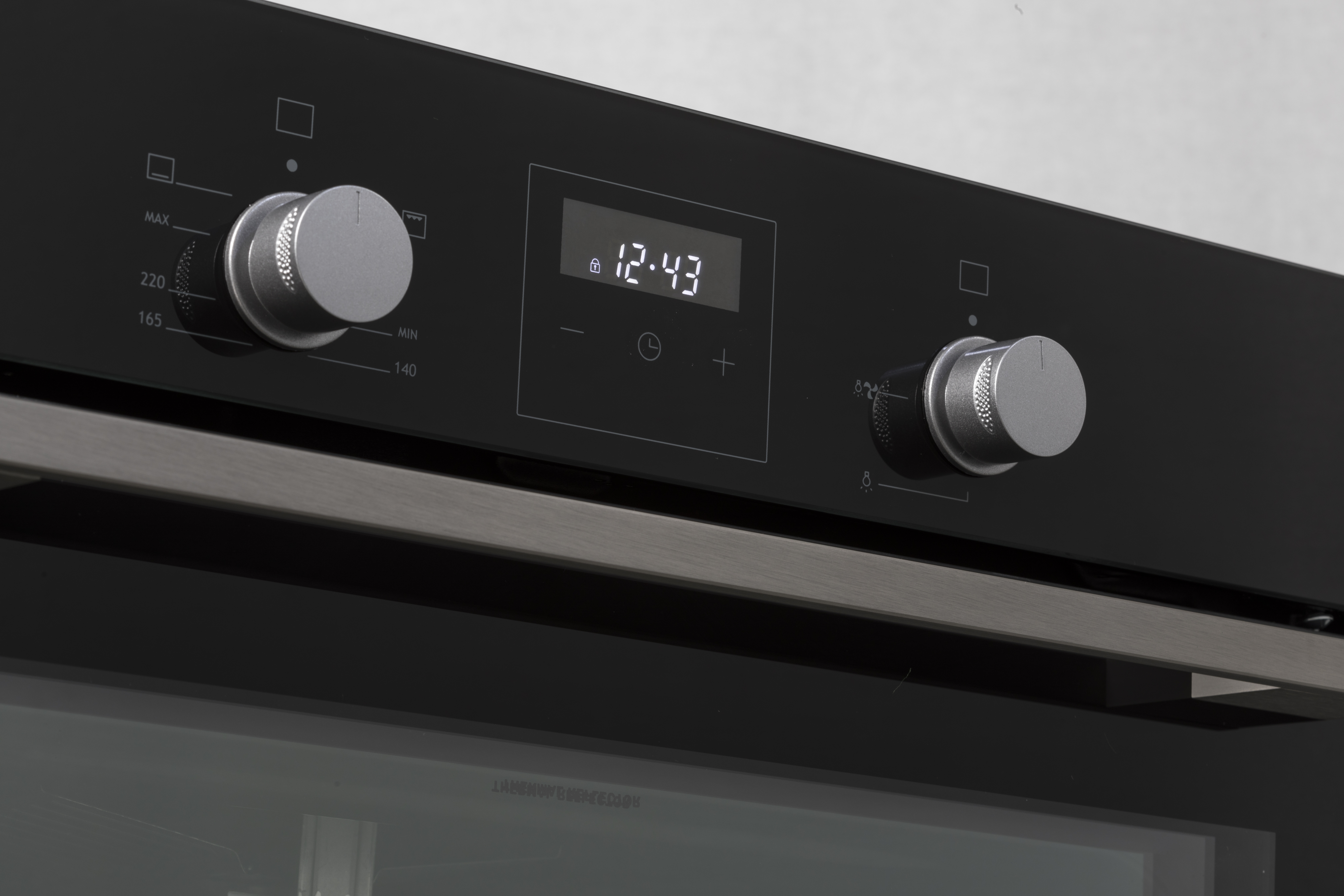 Panel de control del horno con perillas, pantalla y botones. Superficie negra, detalles plateados.