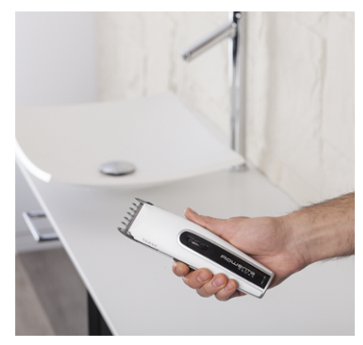 Mano de hombre sosteniendo una afeitadora eléctrica blanca sobre un lavabo blanco. Fondo blanco.