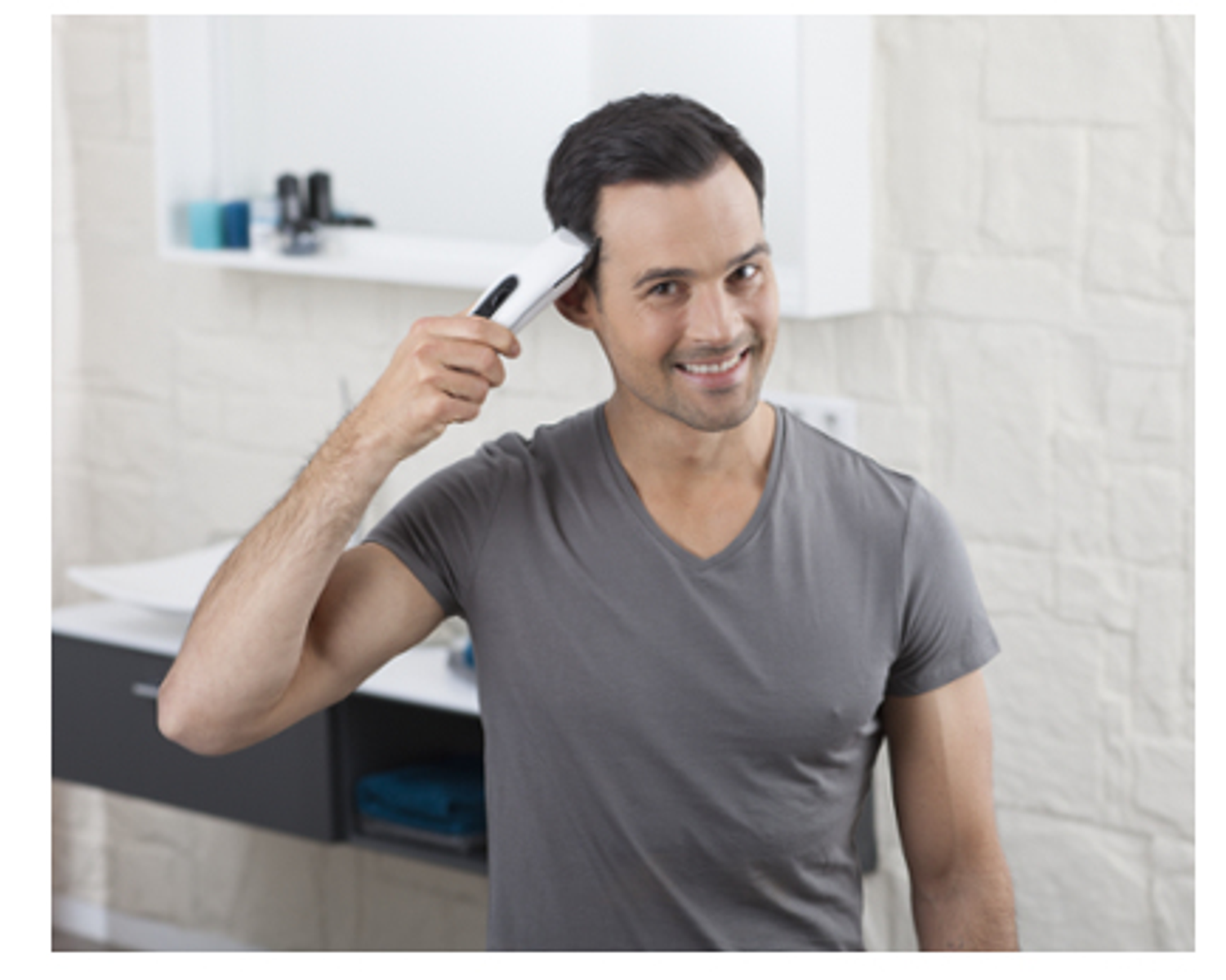 Hombre usando una recortadora de cabello en el baño. Está sonriendo.