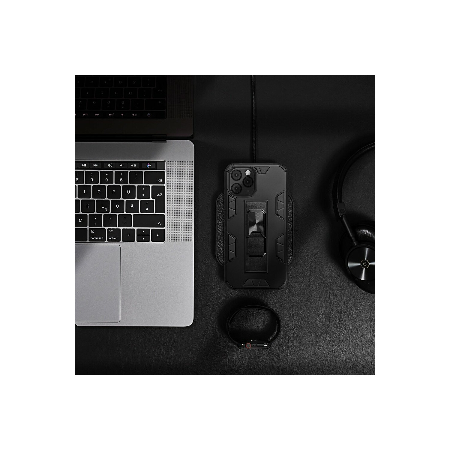 Schwarzes Schreibtisch-Setup: Laptop, Telefon mit Hülle, Kopfhörer und Uhr auf schwarzer Oberfläche.