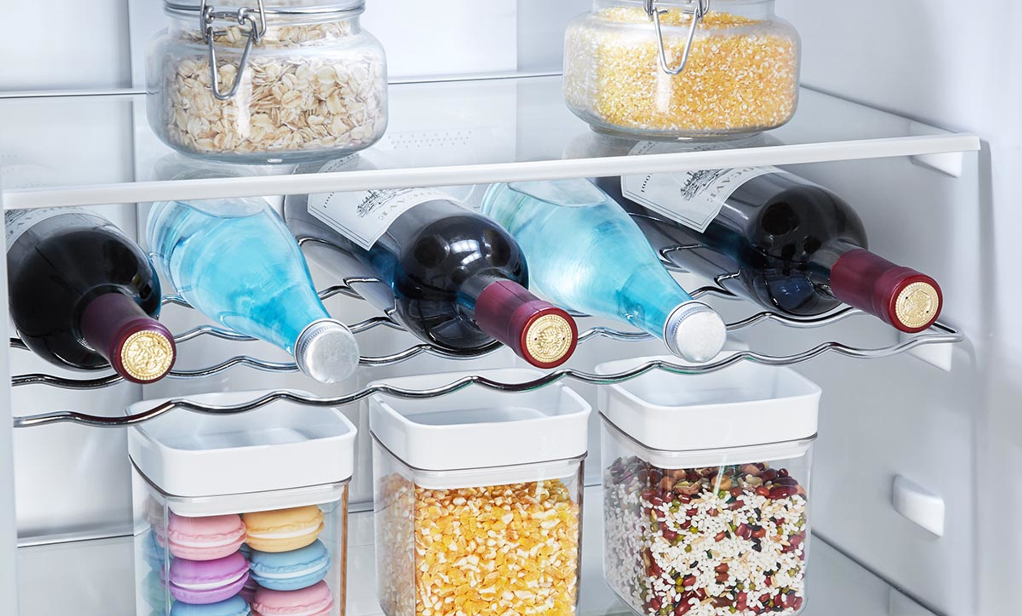 Wewnątrz lodówki: butelki wina, butelki wody i słoiki z jedzeniem na półkach.