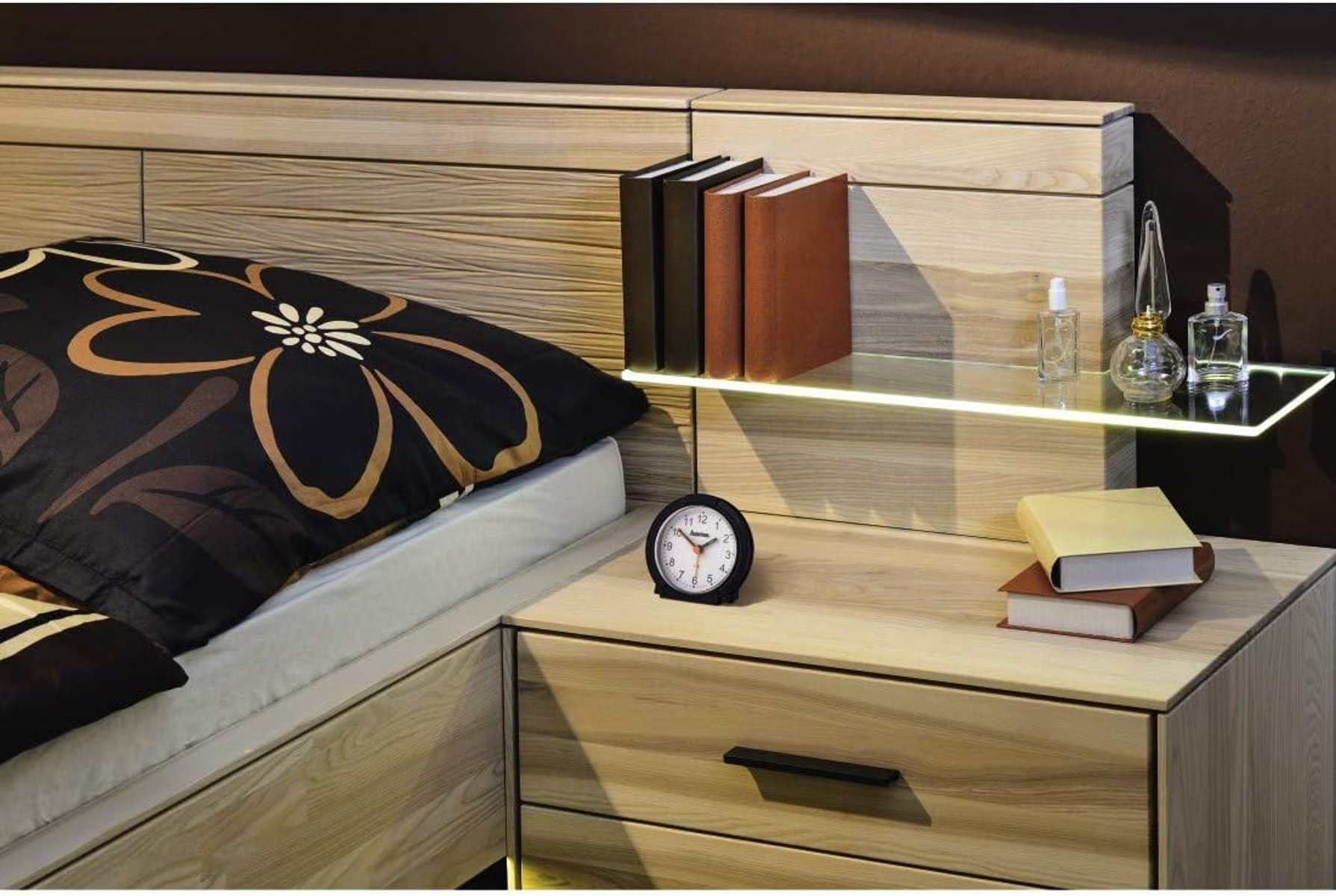 Scena camera da letto con letto, comodino, libri e flaconi di profumo. Illuminazione calda.