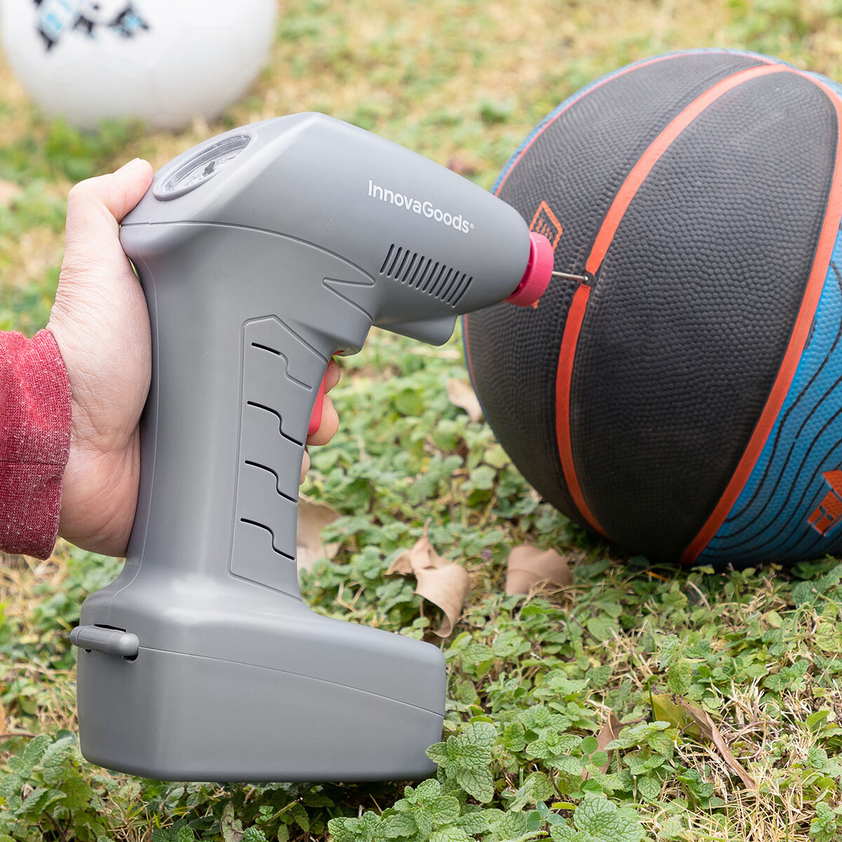 Una pompa ad aria InnovaGoods grigia gonfia un pallone da basket su erba verde.