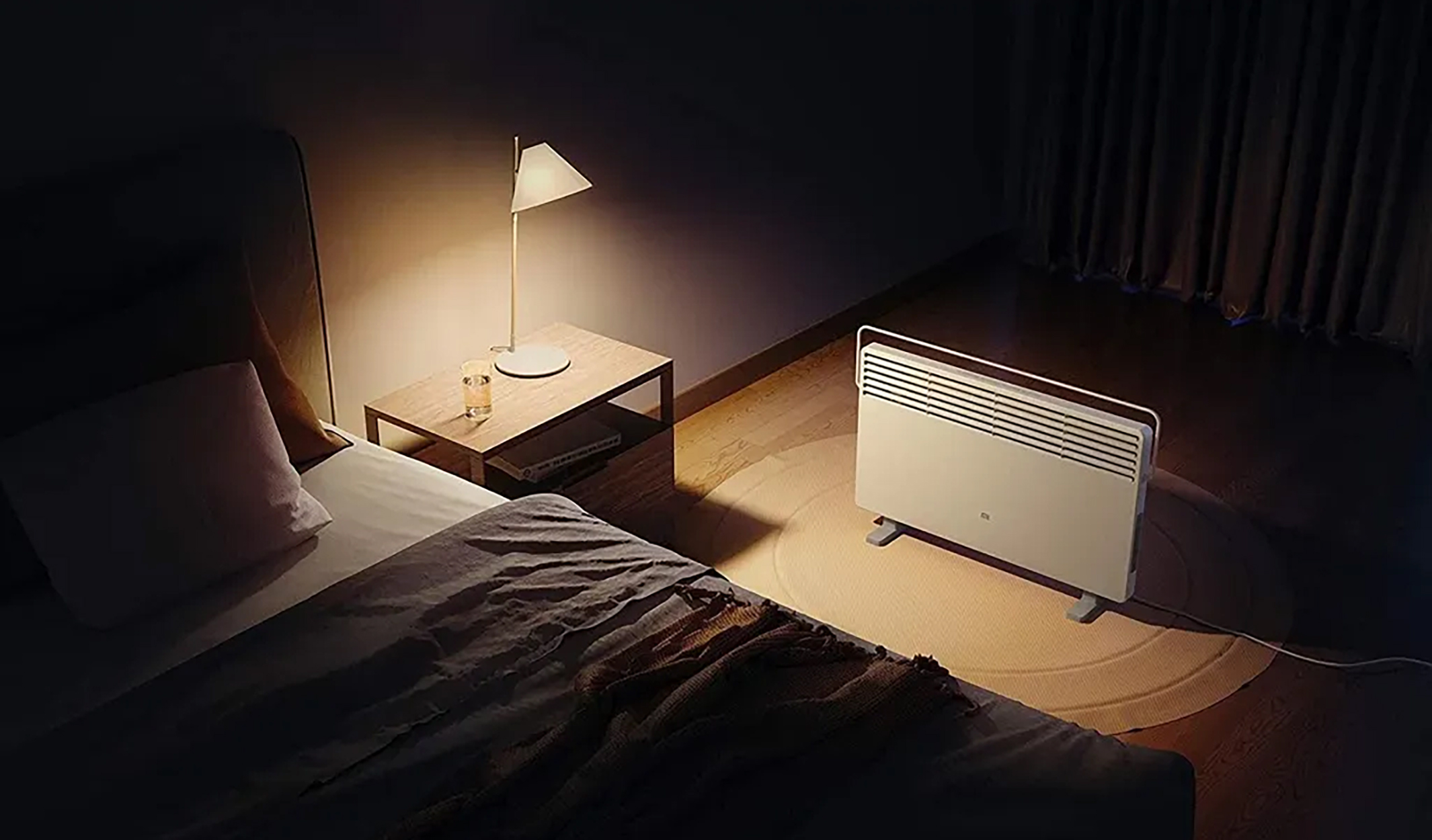 Un dormitorio por la noche con un calefactor y una lámpara. La cama está a la izquierda.