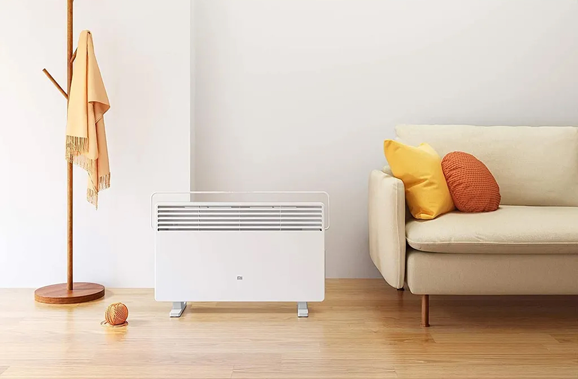 Un calefactor eléctrico blanco en una habitación con un sofá, almohadas y un perchero.