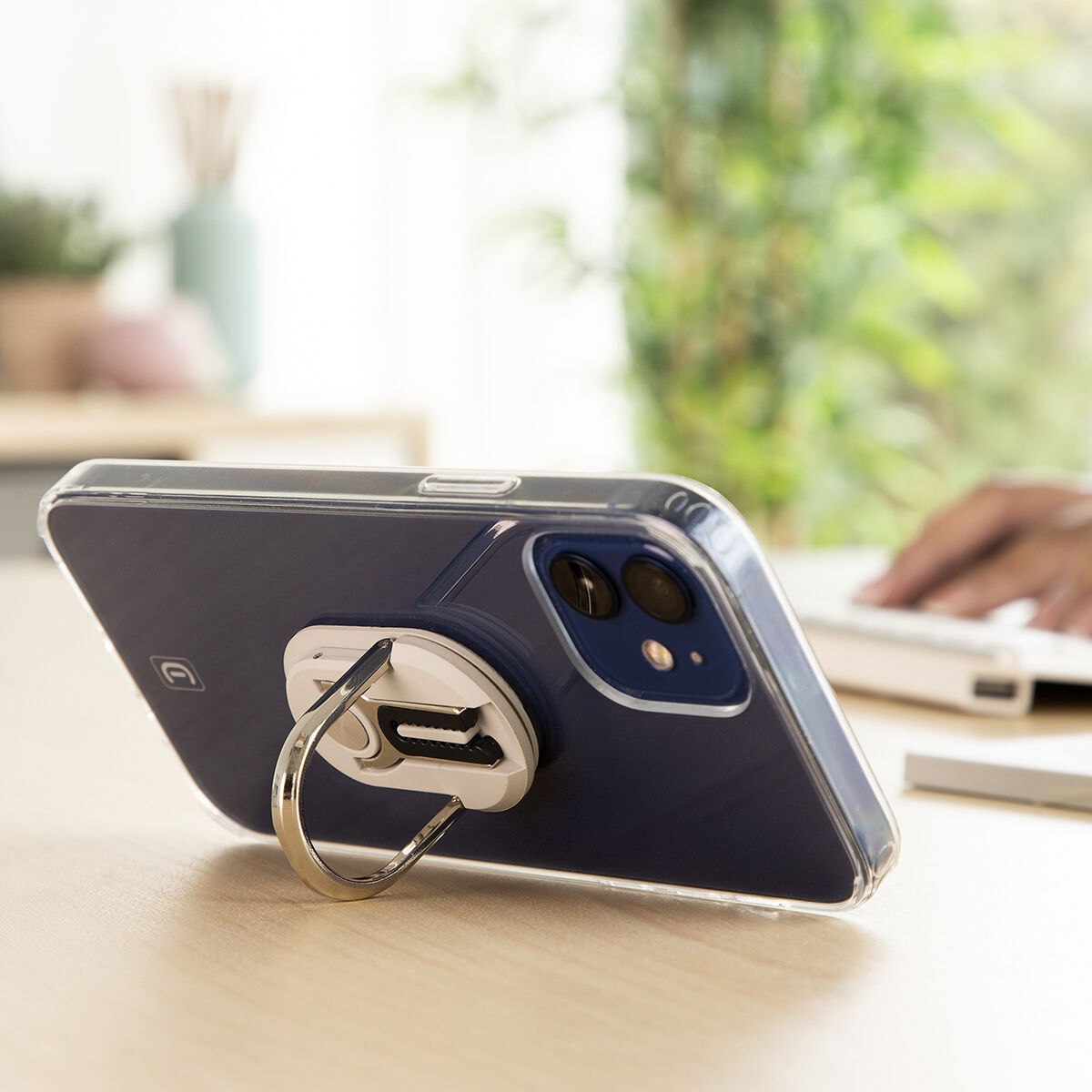 Telefono con anello sul tavolo. La mano di una persona è su un laptop sullo sfondo.